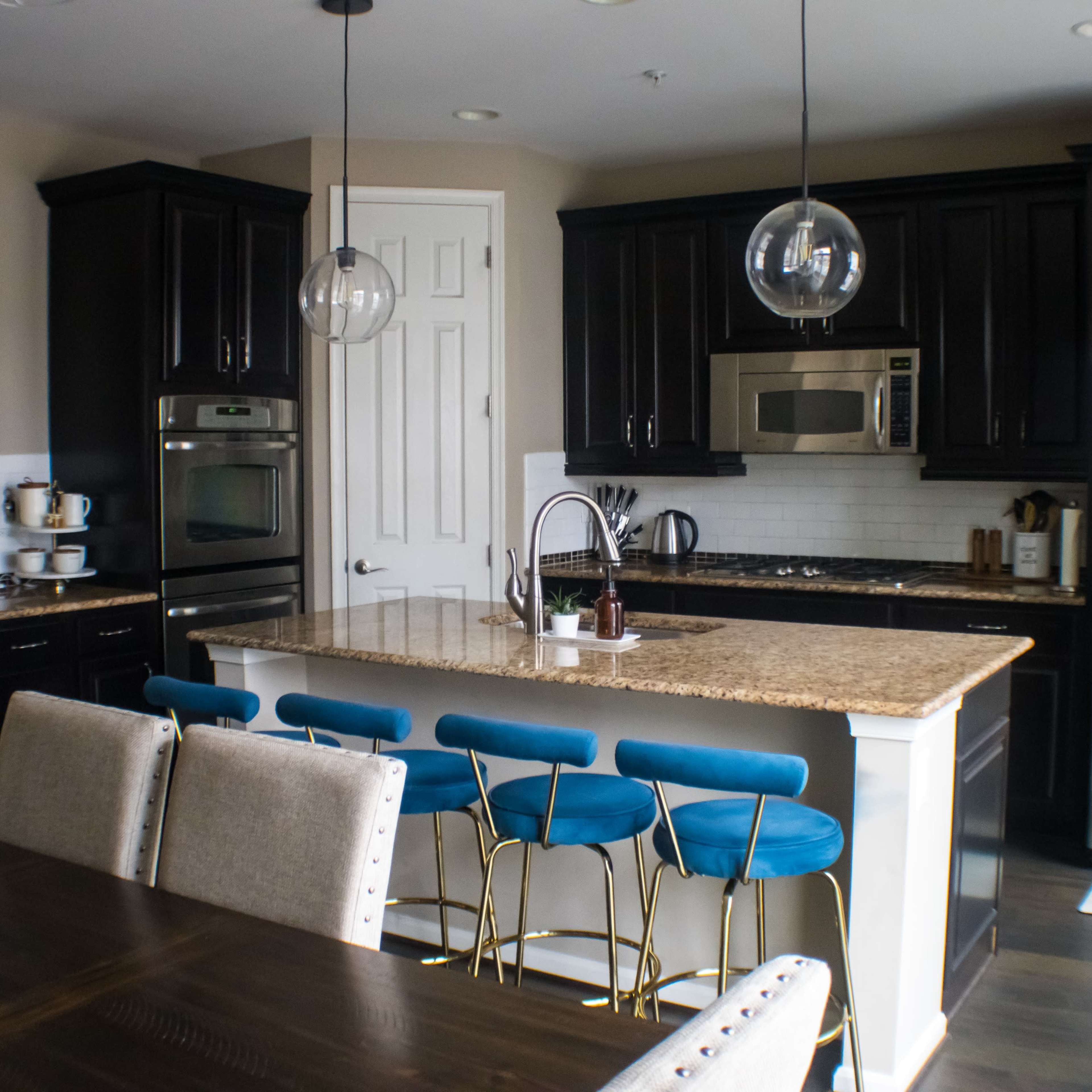 A modern kitchen with dark wooden cabinets, stainless steel appliances, a large granite island, and blue bar stools.