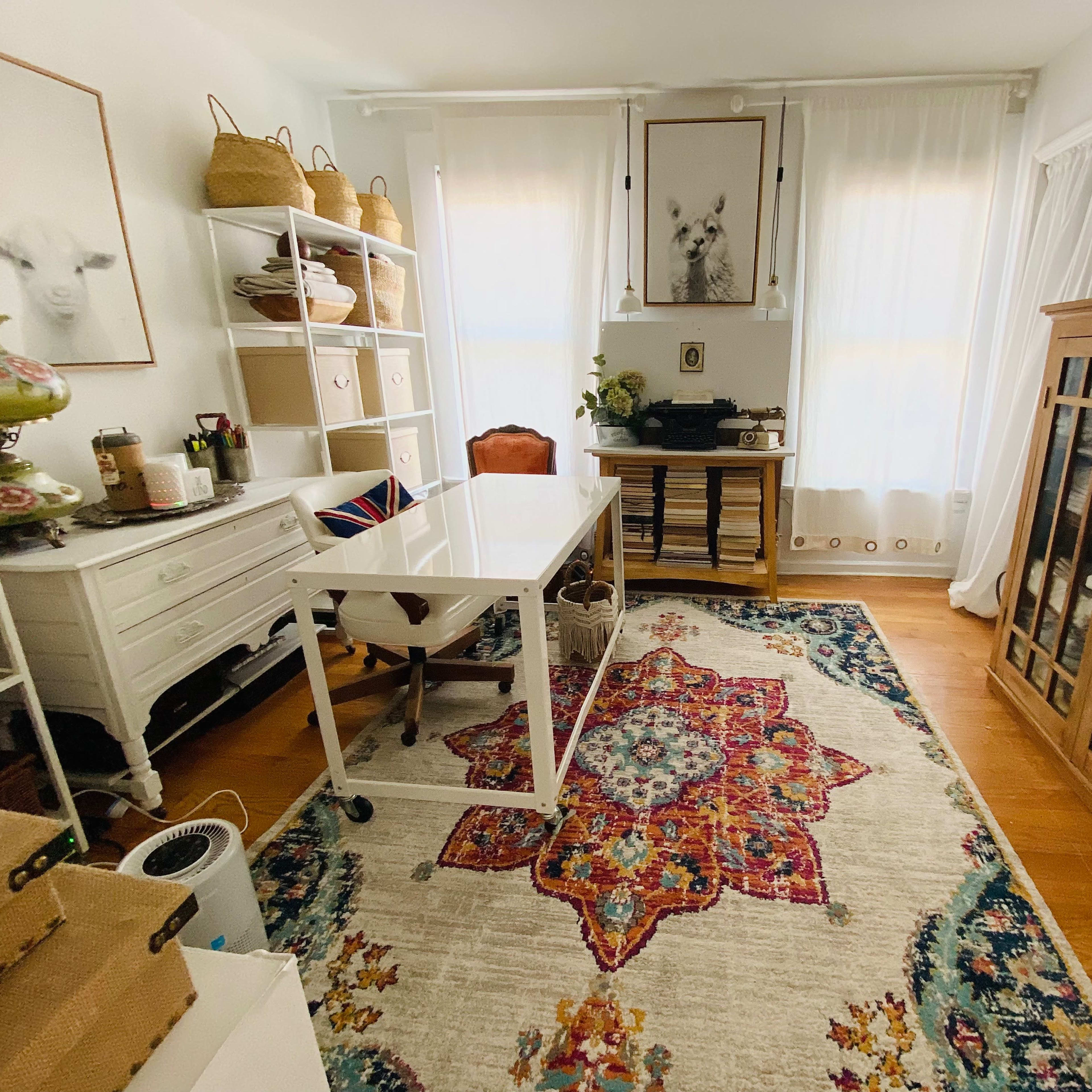 A bright room with a white desk, bookshelf, and a wooden cabinet, all arranged on a colorful patterned rug.