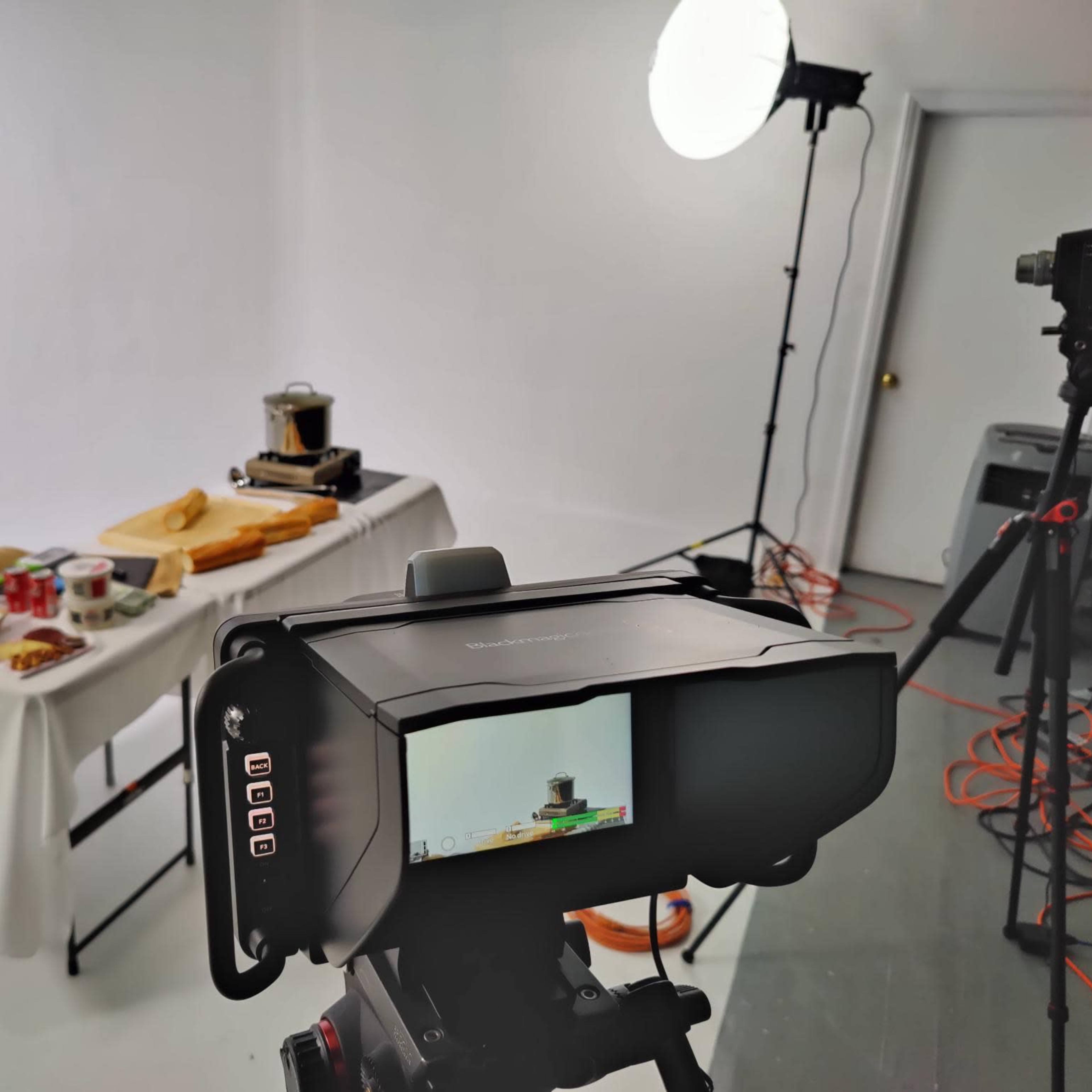 A camera is set up in a studio with a light source, capturing a table displaying various kitchen items and ingredients.
