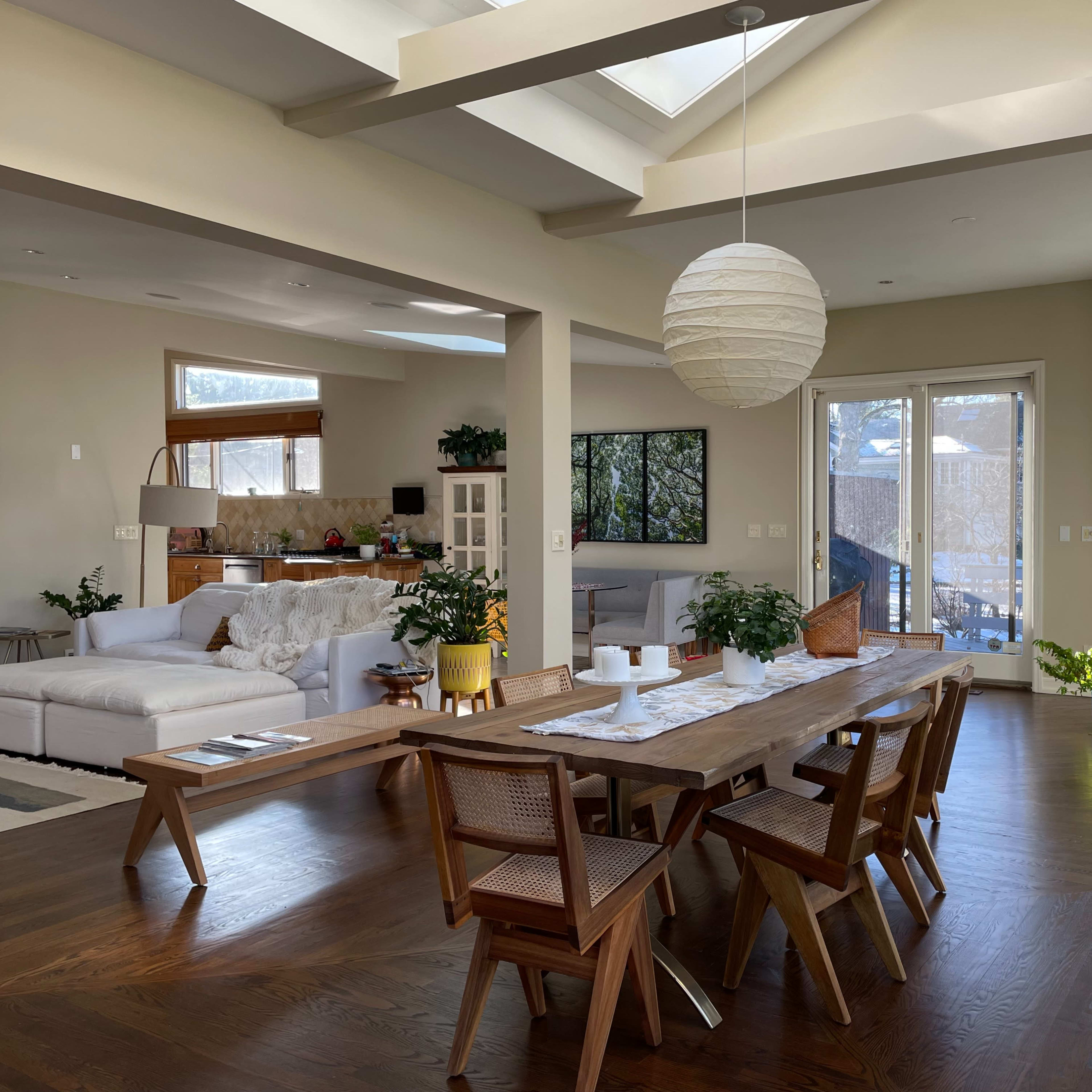 A spacious, open-concept living and dining area features a wooden dining table and a white couch, with large windows that provide ample natural light.