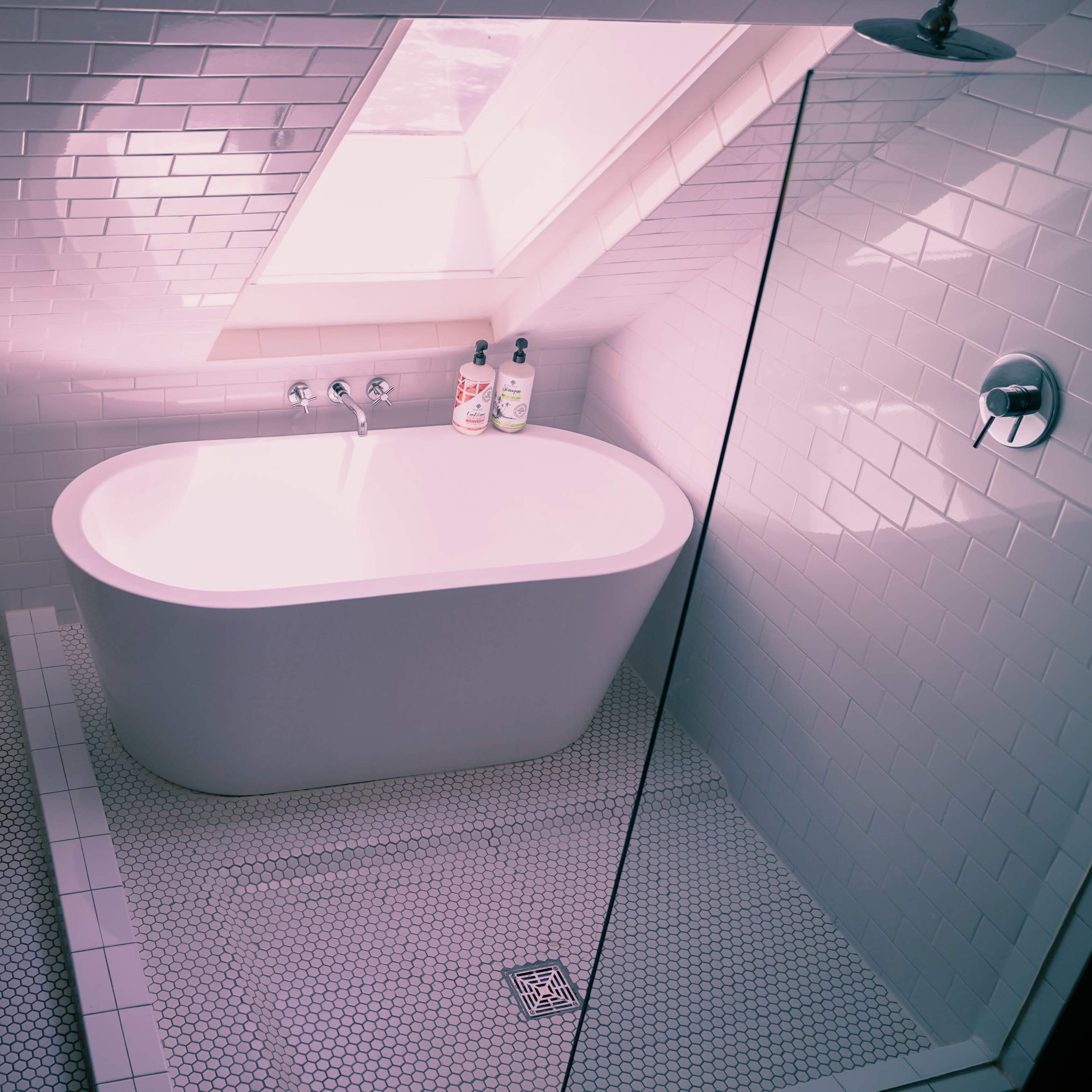 A modern bathroom featuring a freestanding white bathtub, a walk-in shower, and a skylight above.