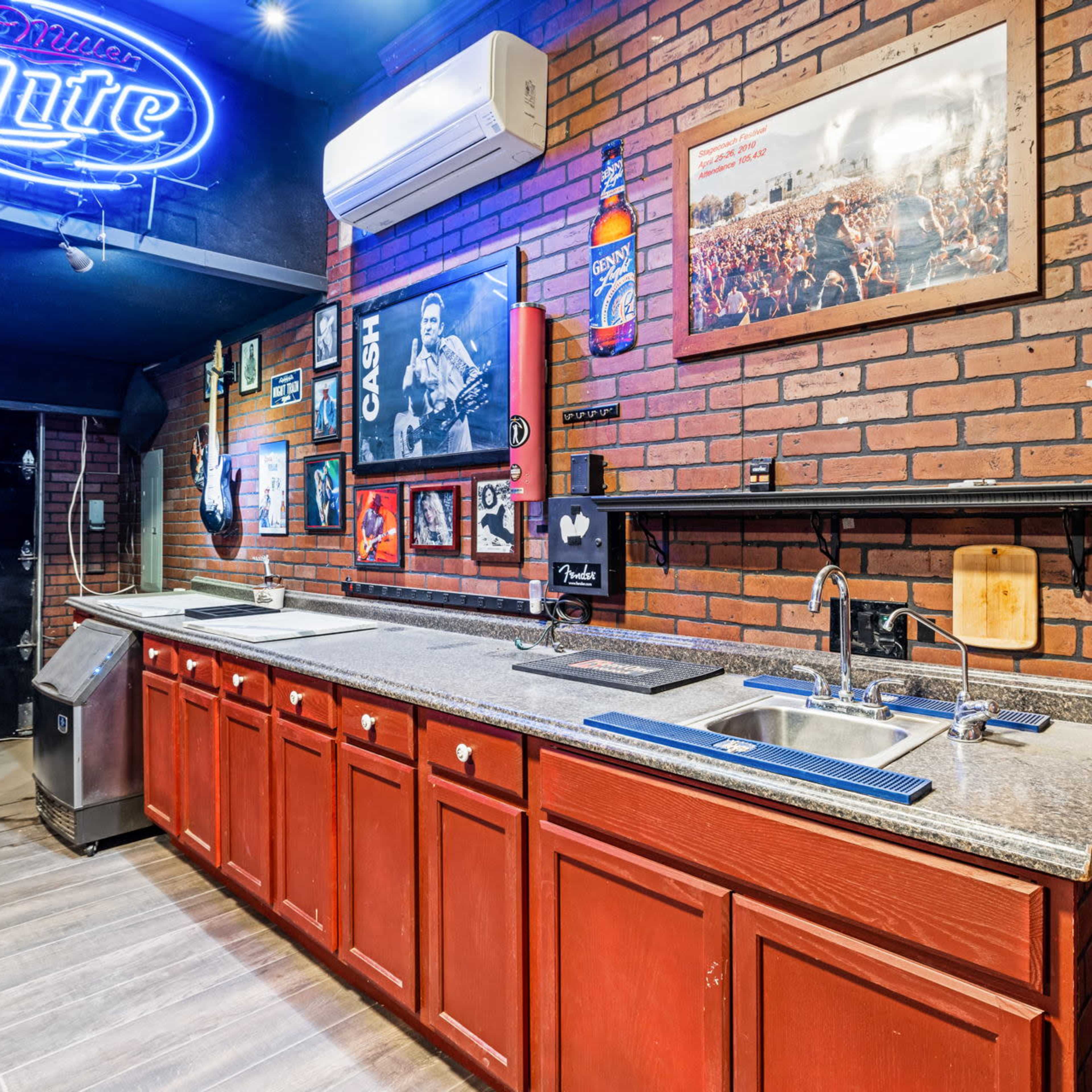 A bar area with a granite countertop, red cabinetry, and brick walls, featuring kitchen sinks and framed photographs.