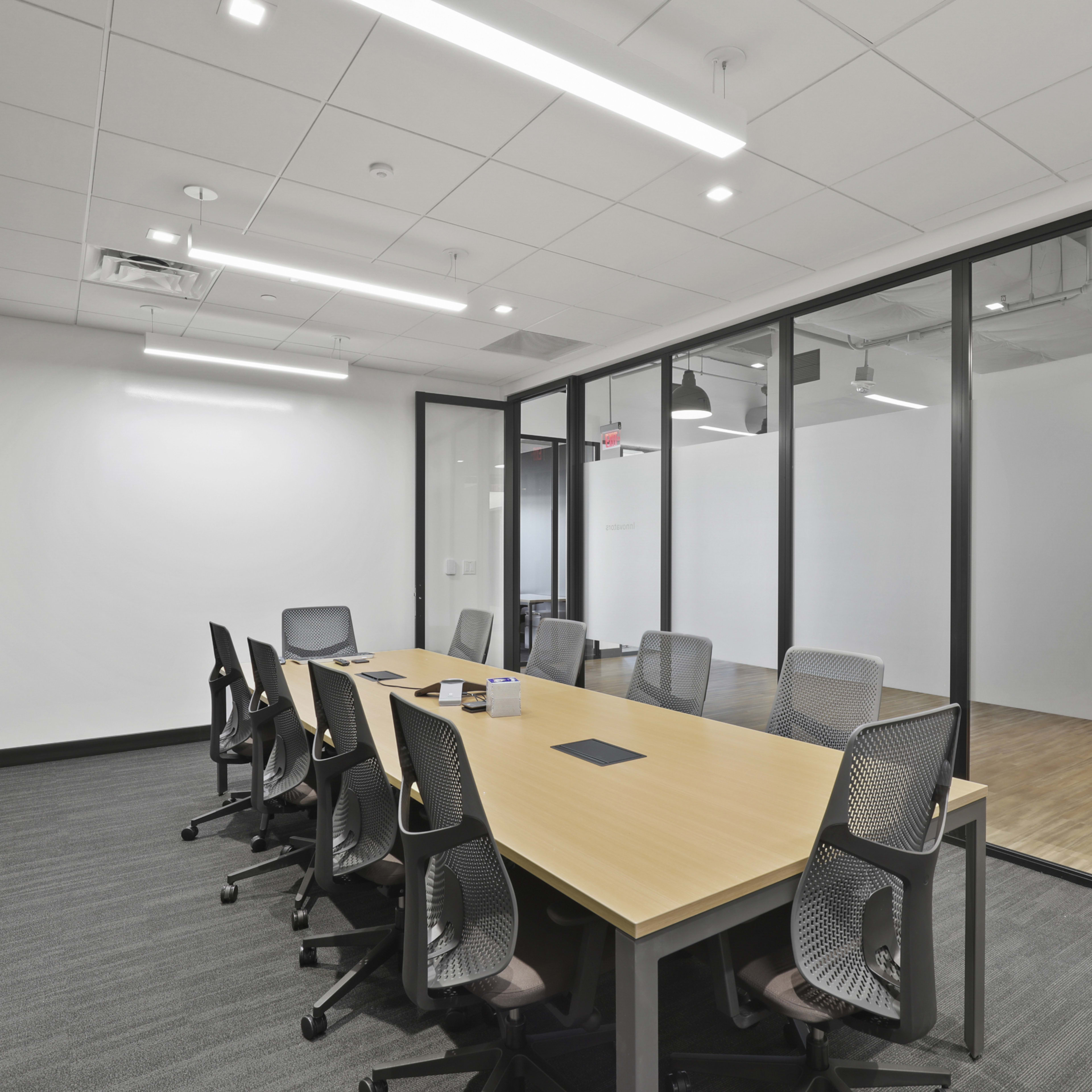 A modern conference room features a large wooden table surrounded by ergonomic chairs, with glass walls separating it from an adjacent space.