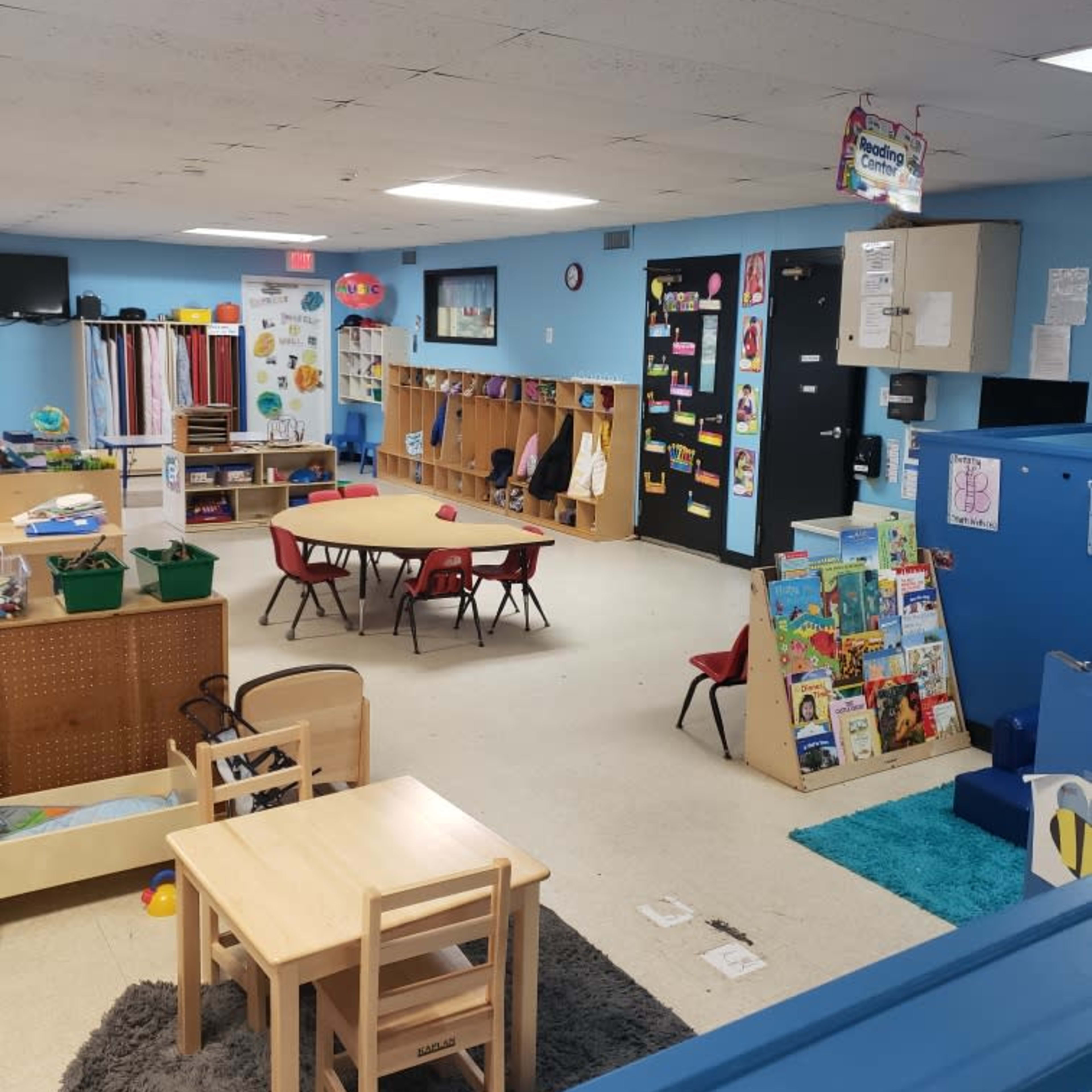 A classroom is arranged with tables and chairs, storage units, and educational materials displayed on the walls.