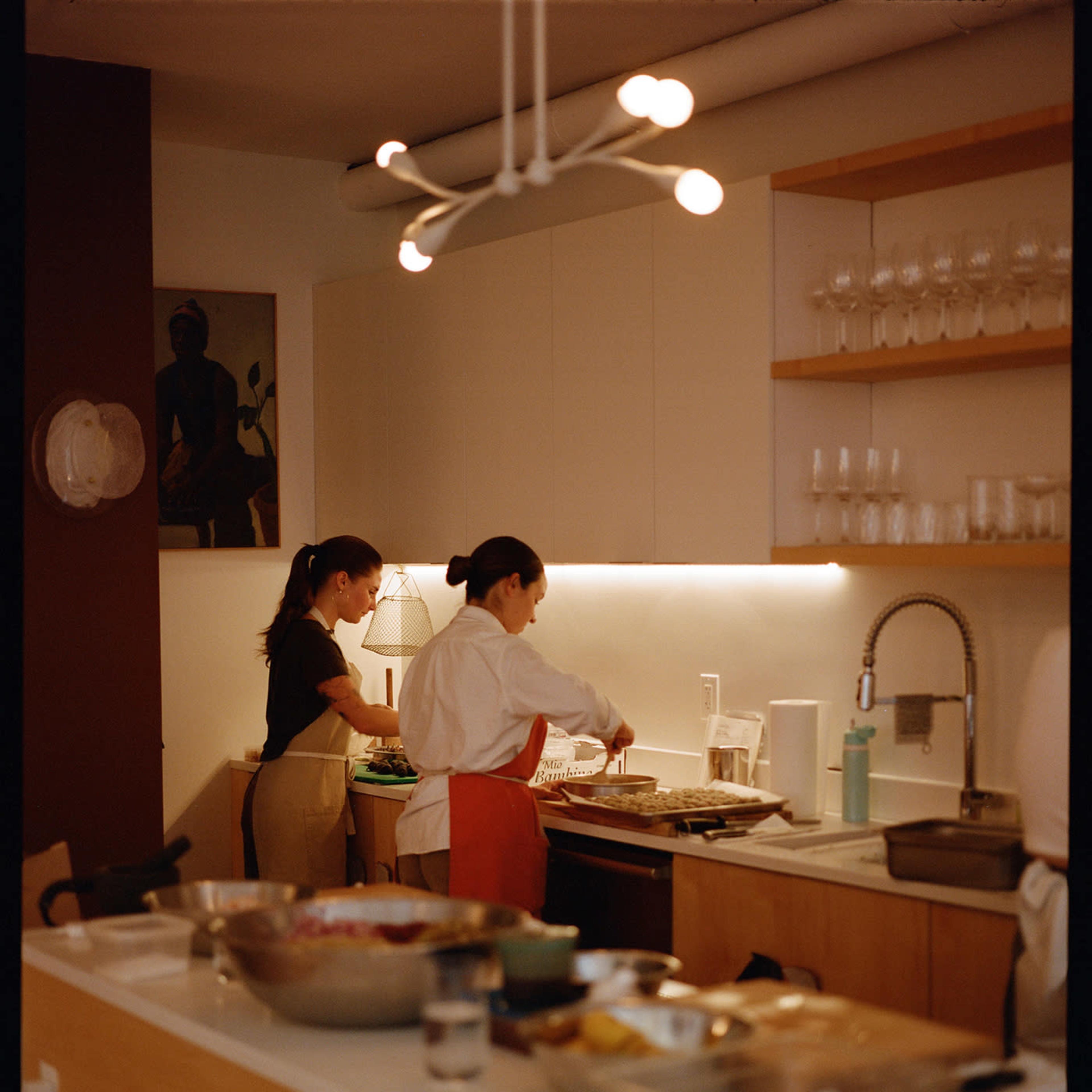 Two individuals are preparing food in a modern kitchen with wooden cabinets and a white countertop.