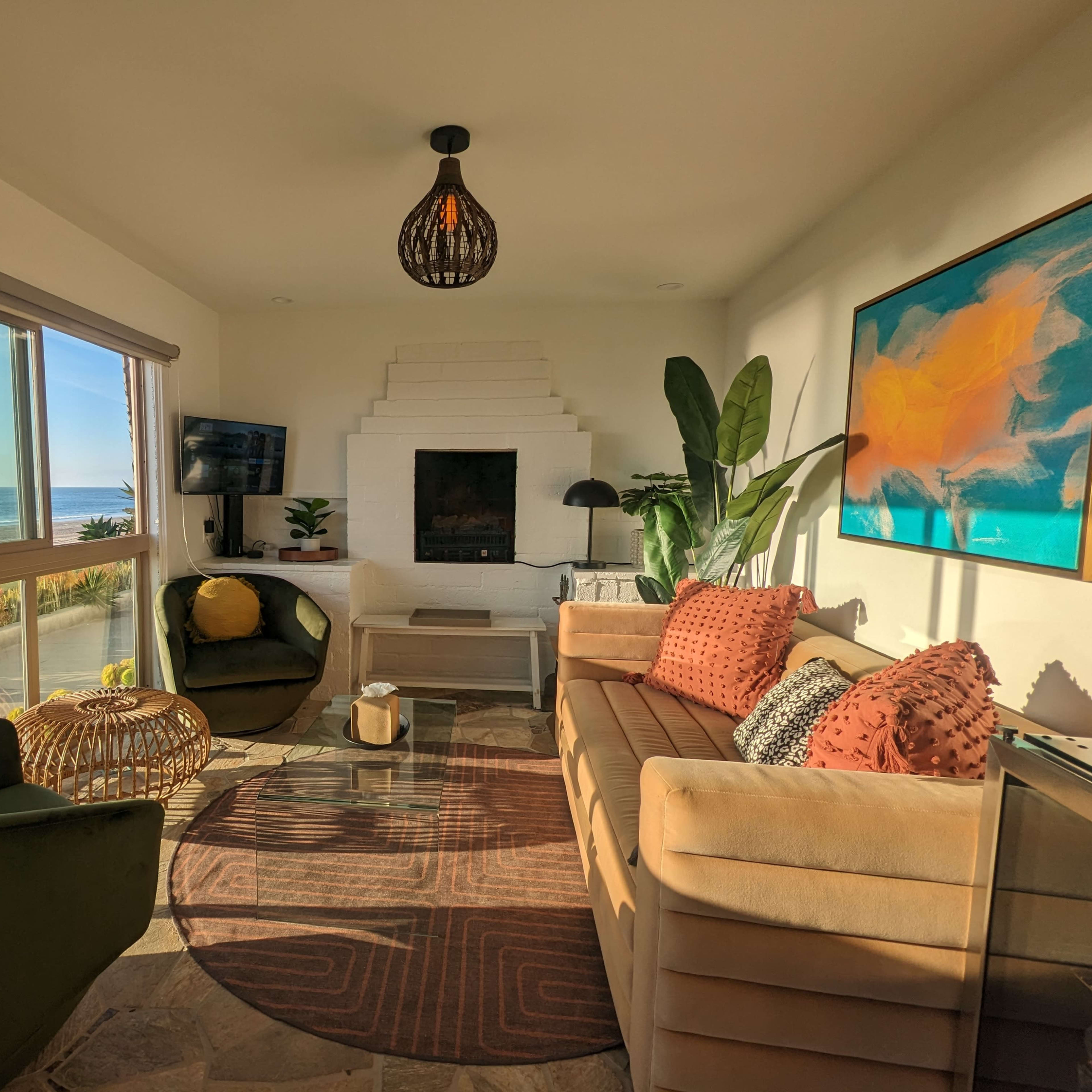 A modern living room with a view of the ocean, featuring a sofa, two green chairs, a coffee table, and a large window letting in natural light.