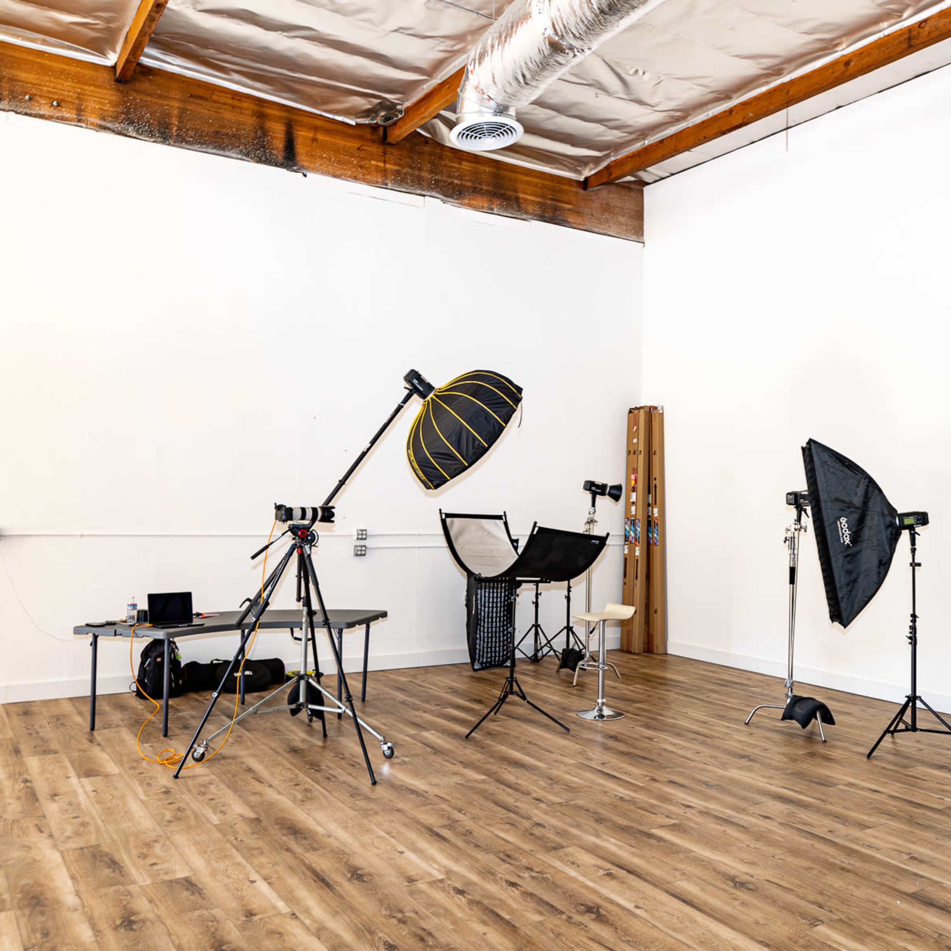 A photography studio with various lighting equipment, a table, and backdrops set against a plain wall and wooden floor.