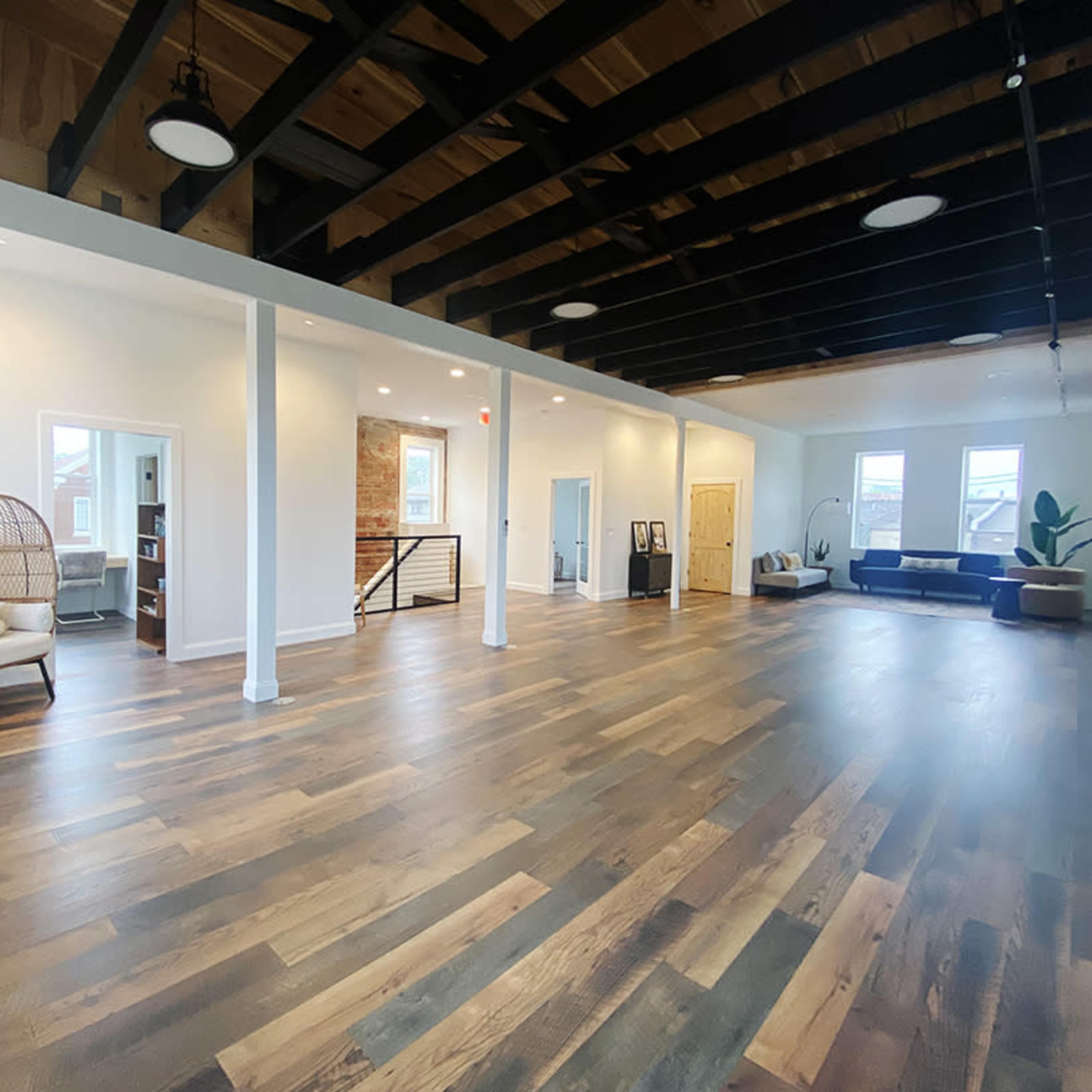 An open, spacious interior with hardwood flooring, exposed beams, and a mix of seating areas, including a wicker chair and a sofa.