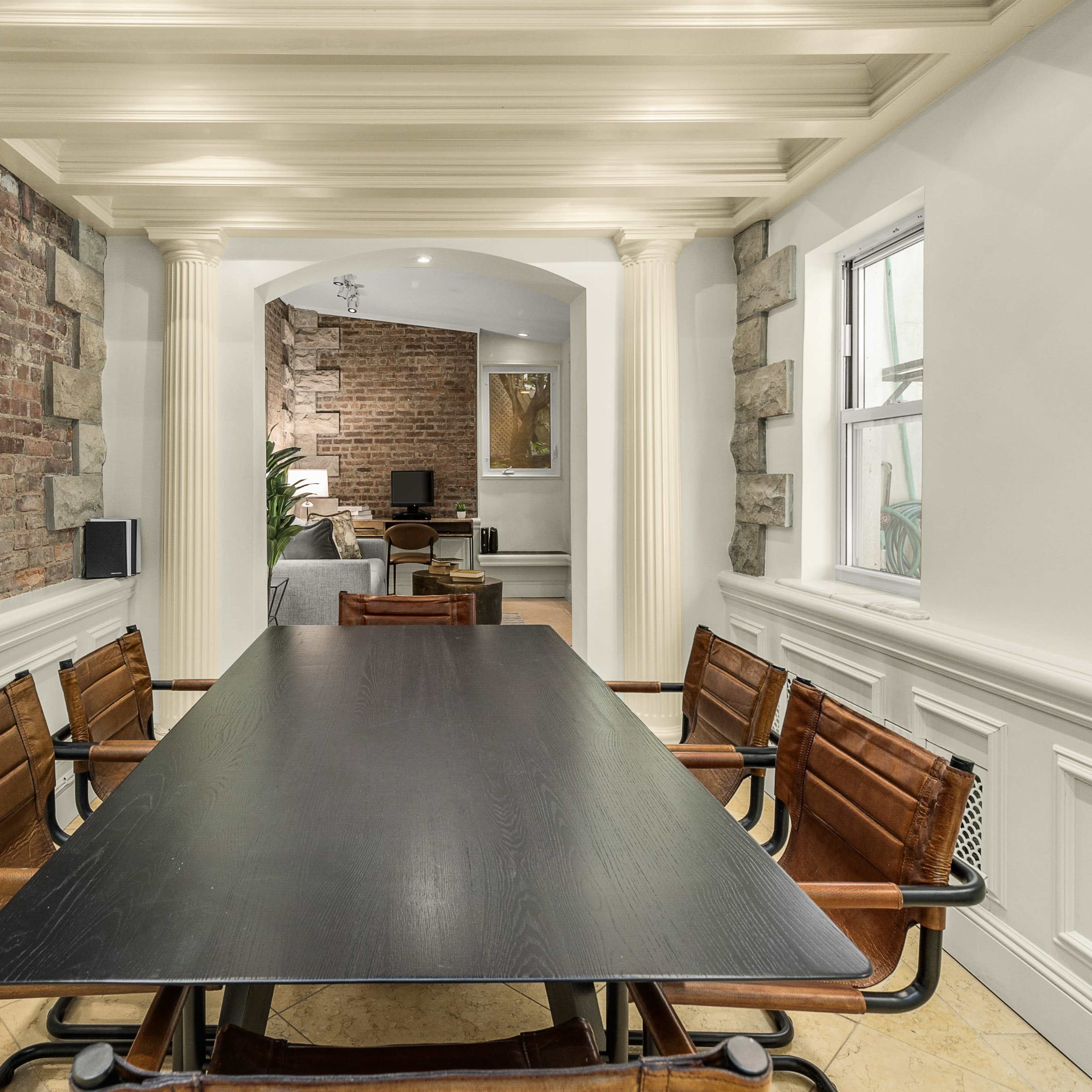 A long black table with leather chairs is set in a room with exposed brick walls and elegant architectural details.