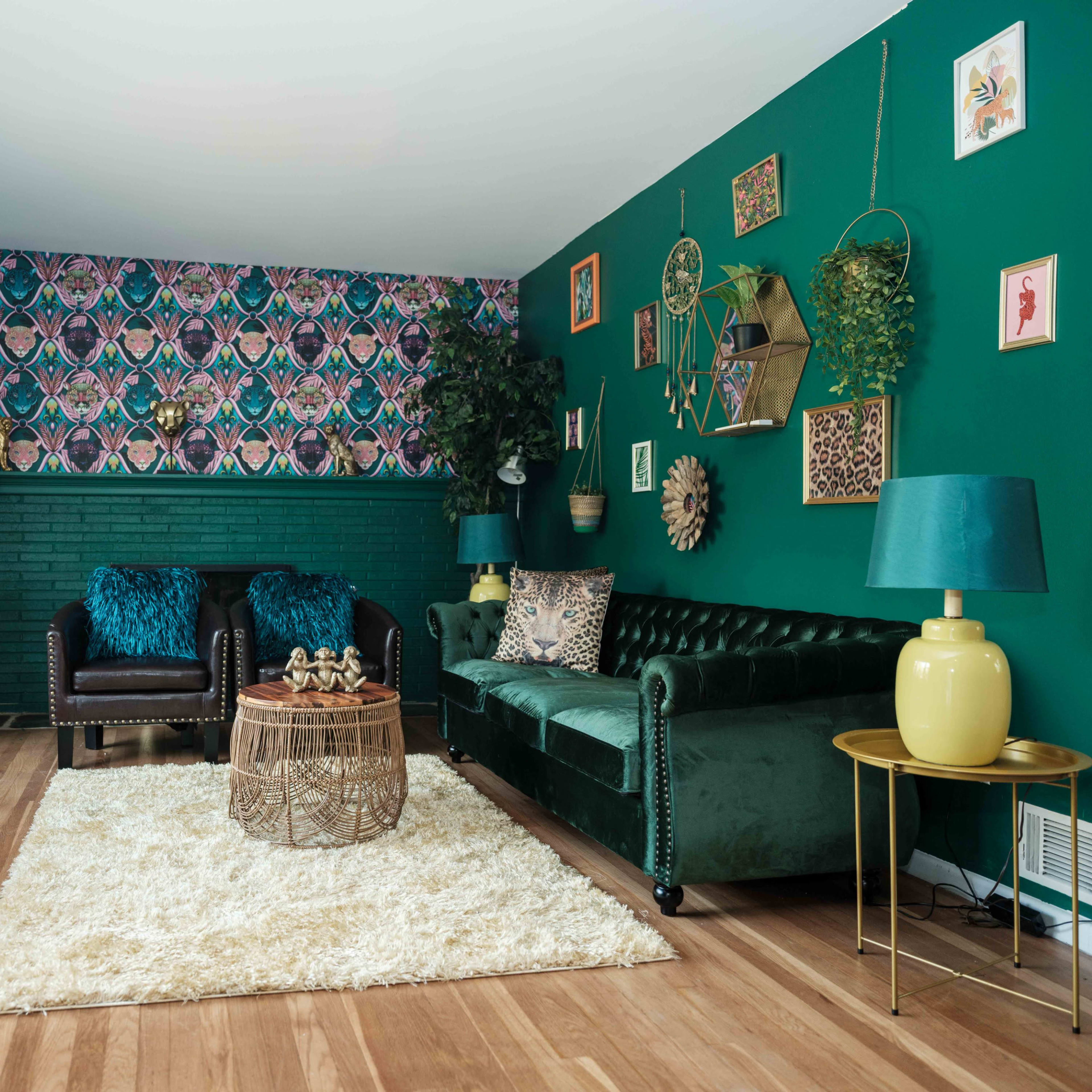 A living room features a green color scheme with a patterned accent wall, a plush rug, and various plants arranged on the walls.
