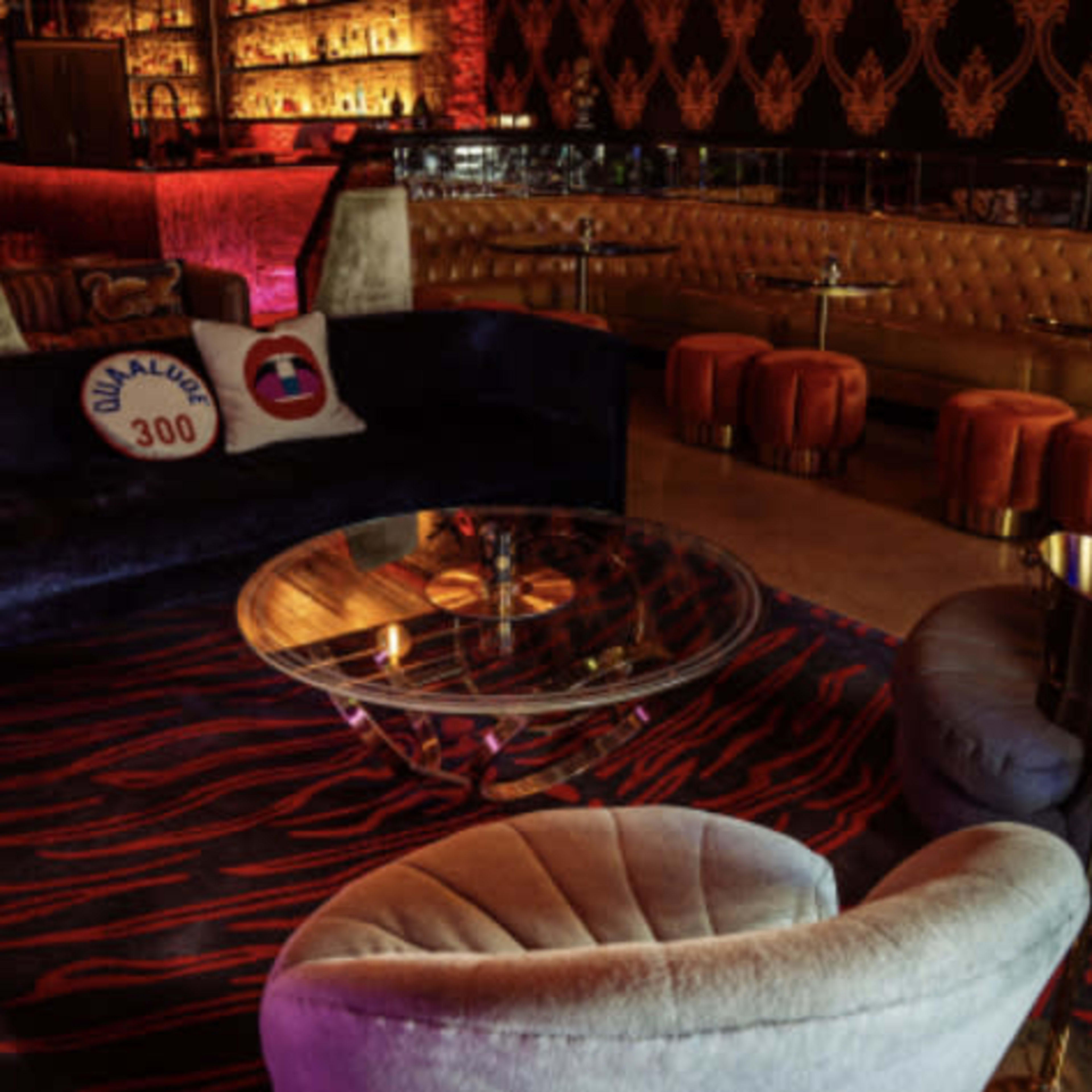 A stylish lounge area with a plush velvet sofa, two upholstered chairs, a glass coffee table, and a patterned rug, all set against an elegantly decorated backdrop.