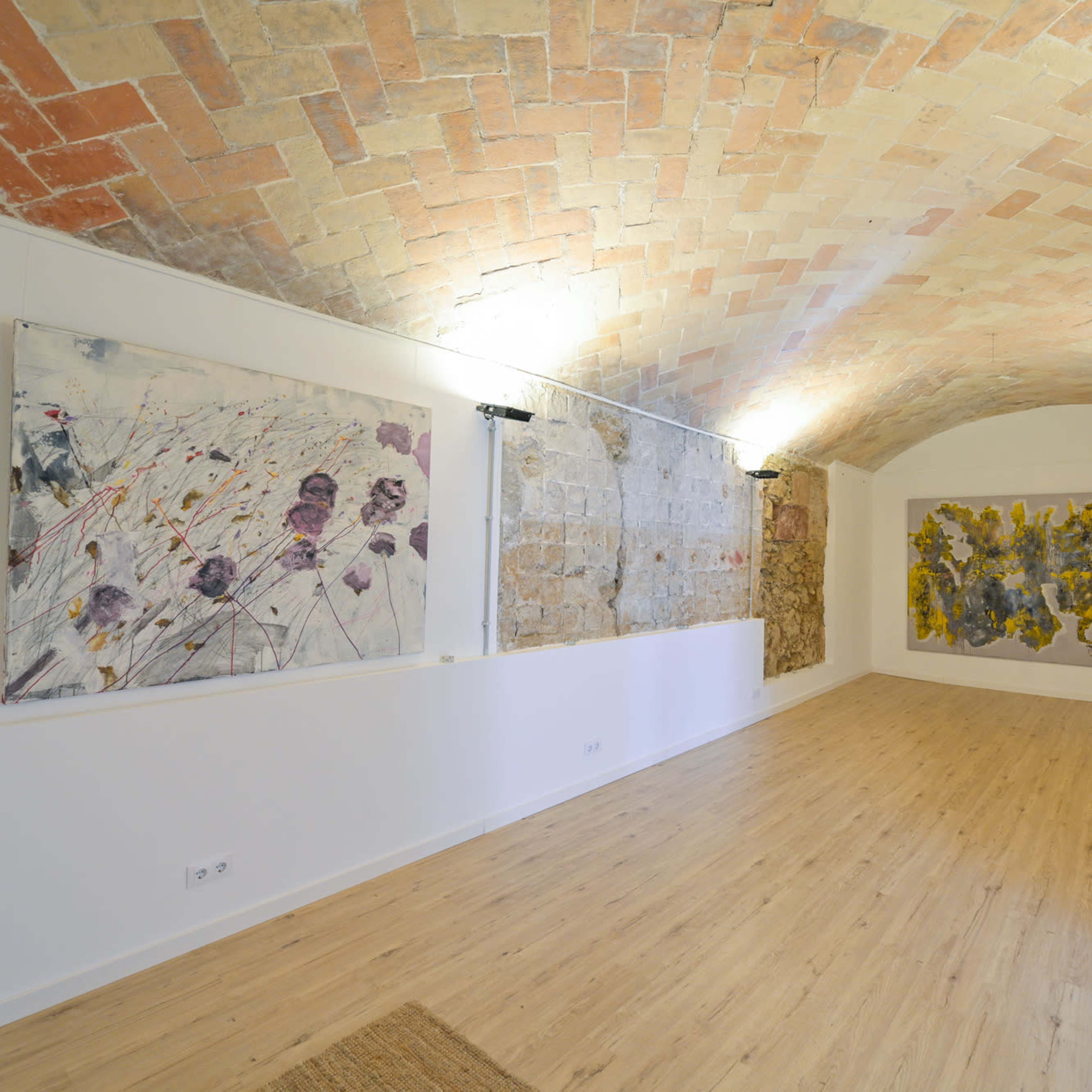 An art gallery with a curved brick ceiling, featuring two large paintings on the walls and wooden flooring.
