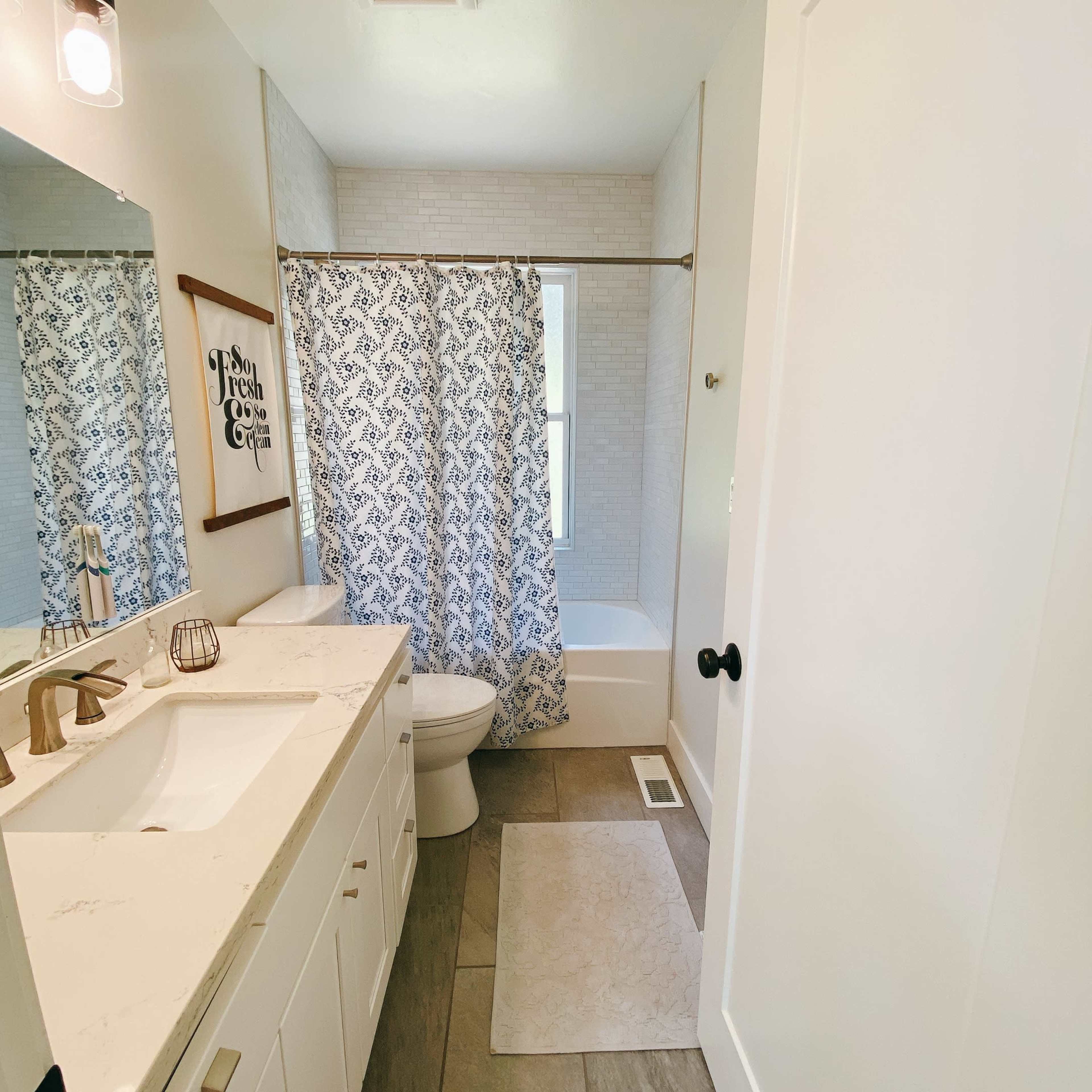 A bathroom features a bathtub with a shower curtain, a sink with a countertop, and a window letting in natural light.