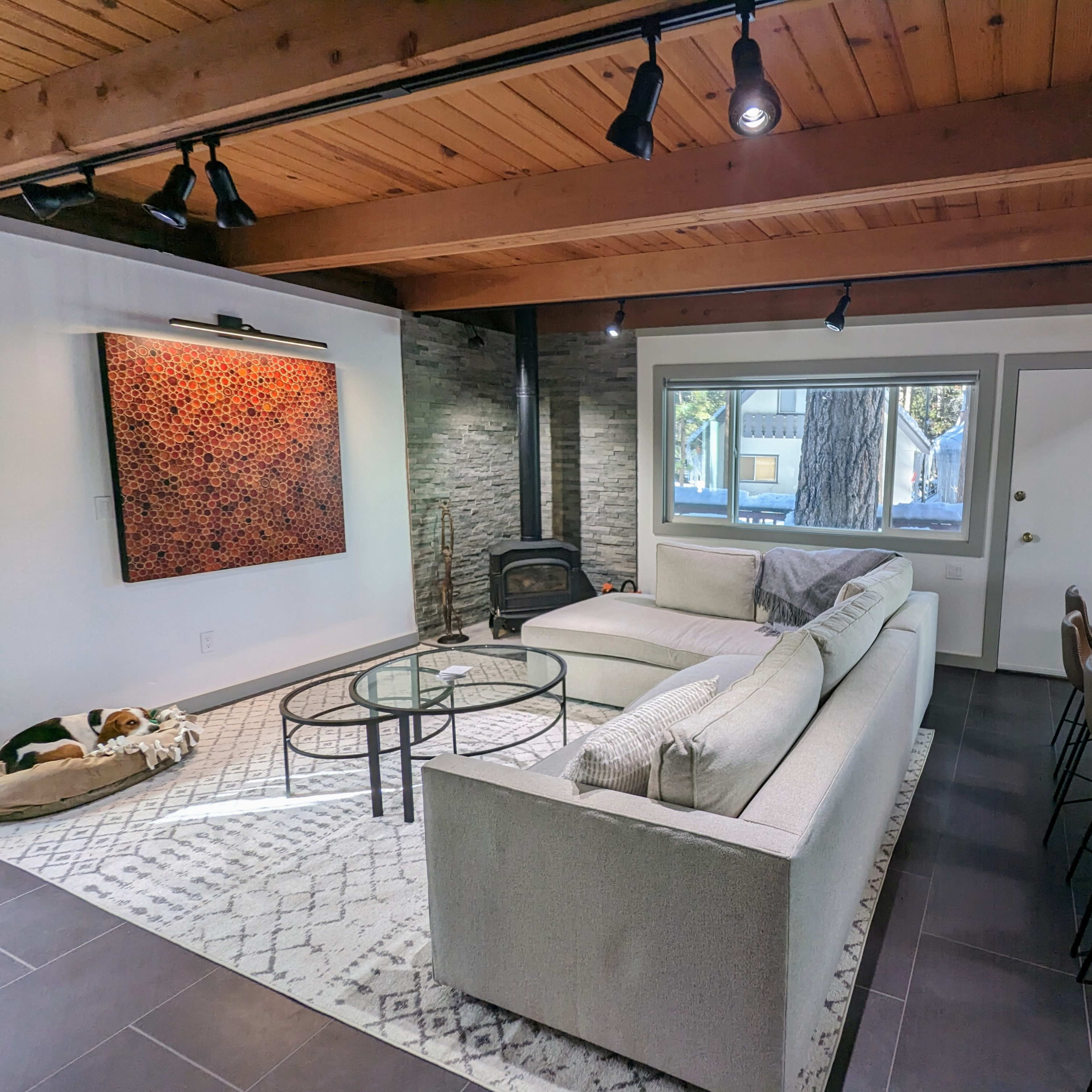 A modern living room with a sectional sofa, a glass coffee table, a stone fireplace, and a dining area featuring a wooden counter with bar stools.
