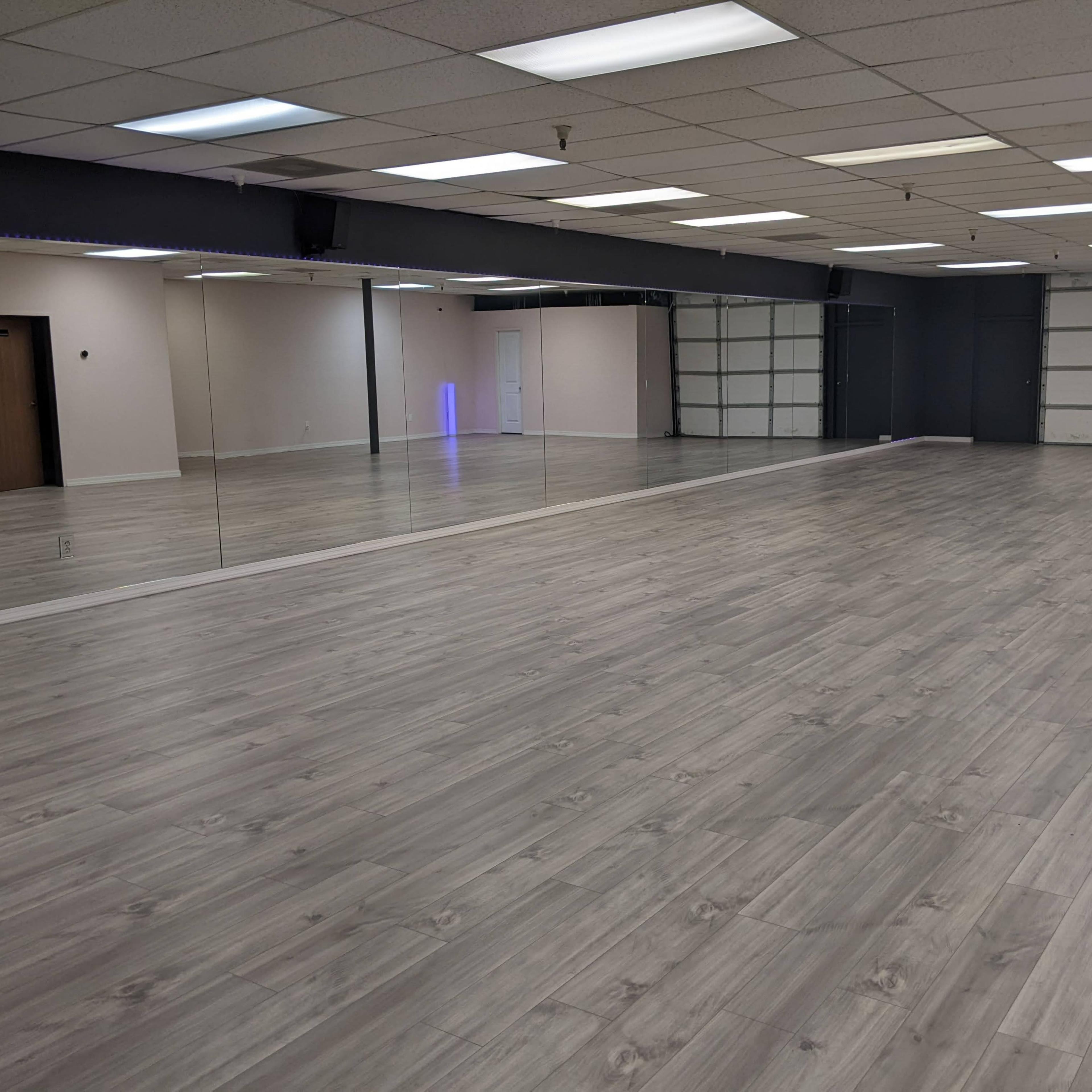 A spacious, empty room with gray wooden flooring and large mirrors on one wall.