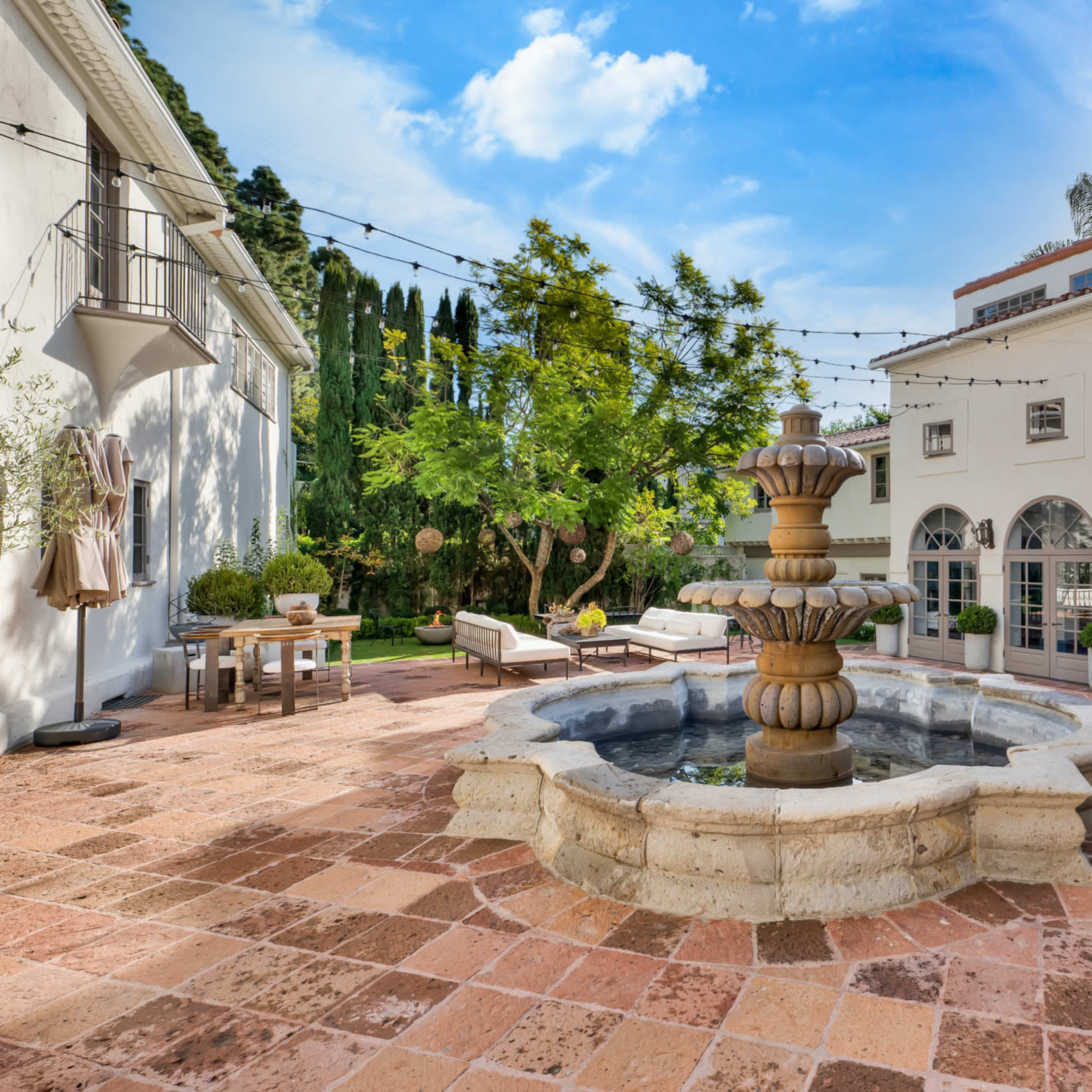 A stone fountain creates a central feature in a brick patio surrounded by lounge chairs and greenery.
