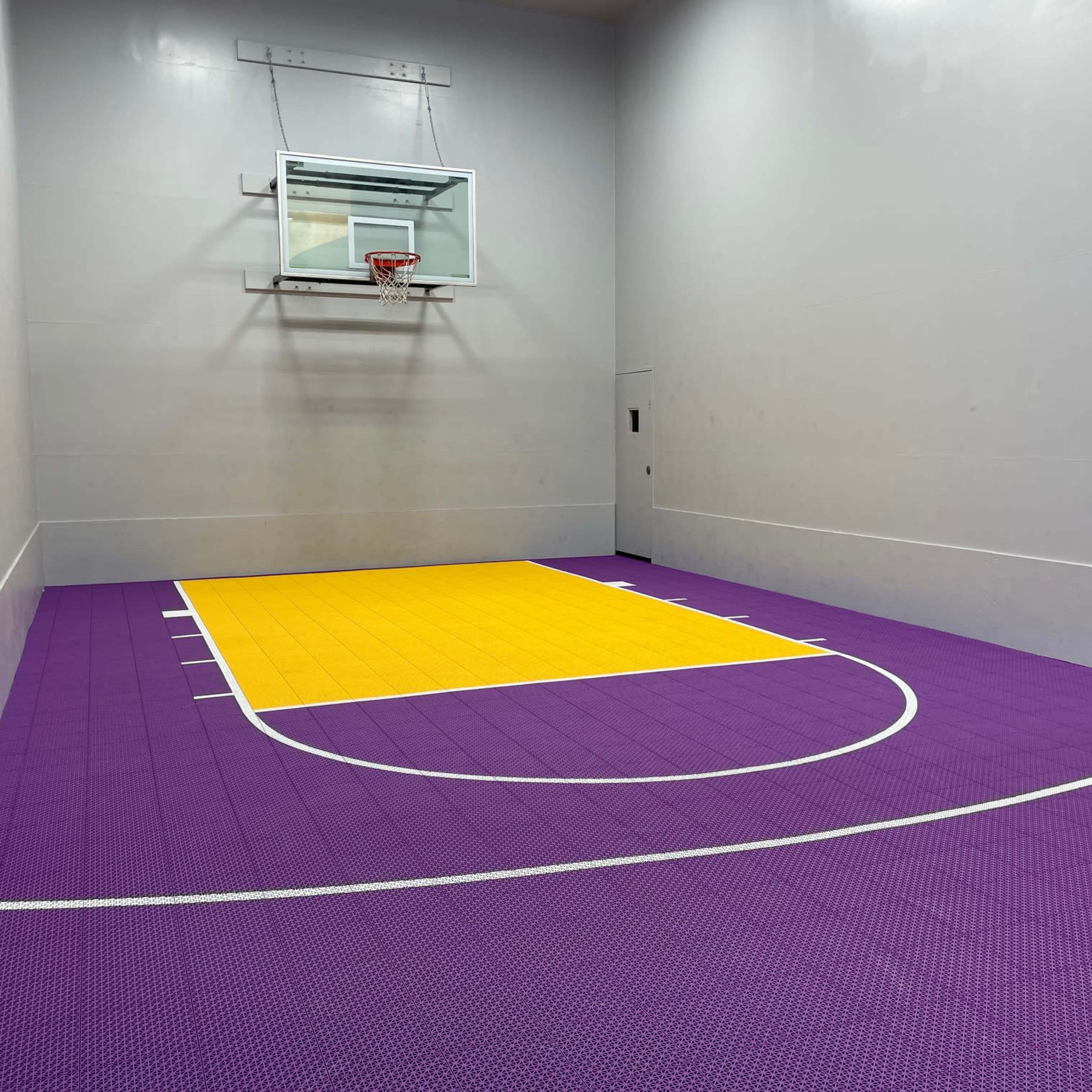 A small indoor basketball court with a yellow and purple floor and a basketball hoop mounted on a gray wall.