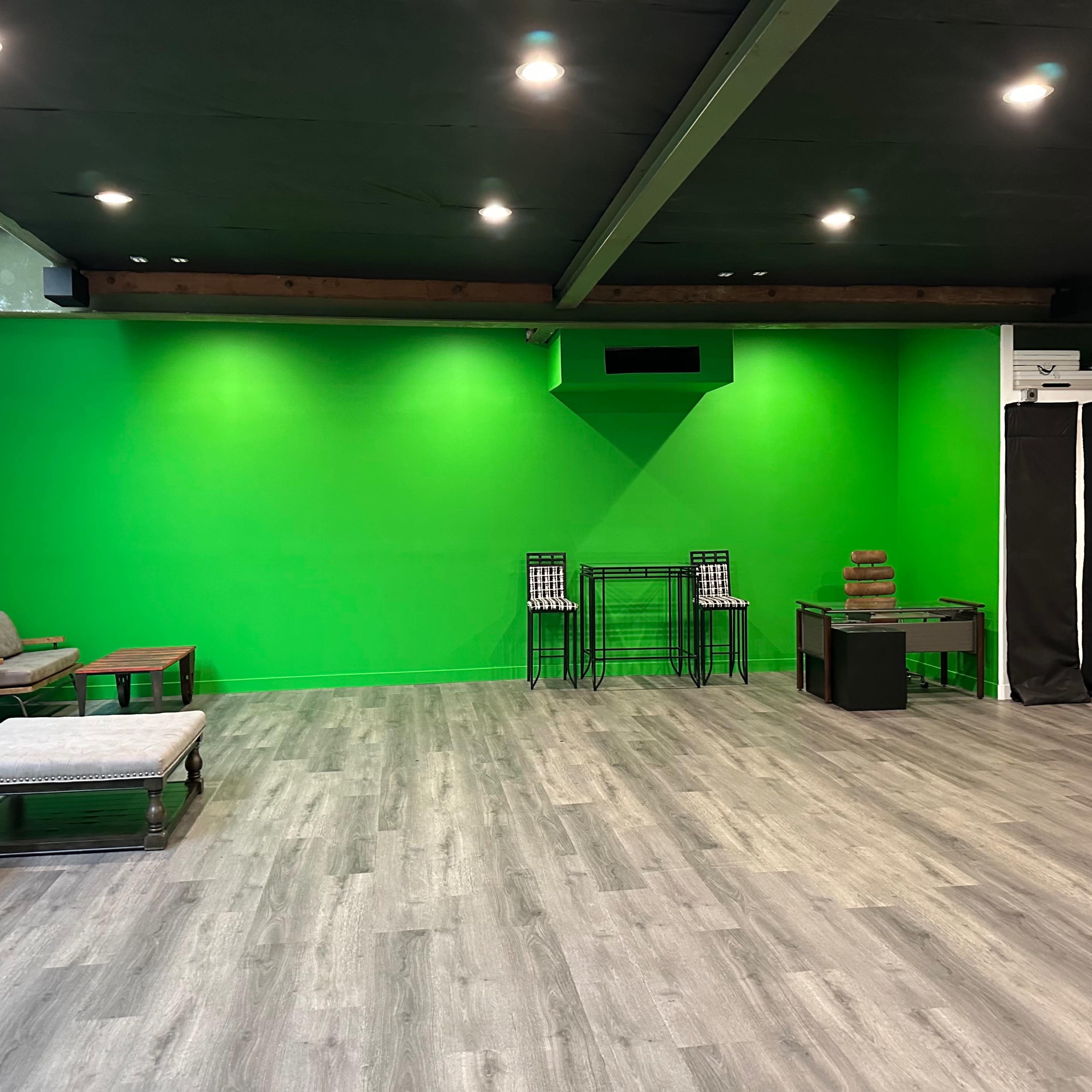 A spacious interior with a green backdrop, hardwood-like flooring, and a few minimalist furniture pieces.