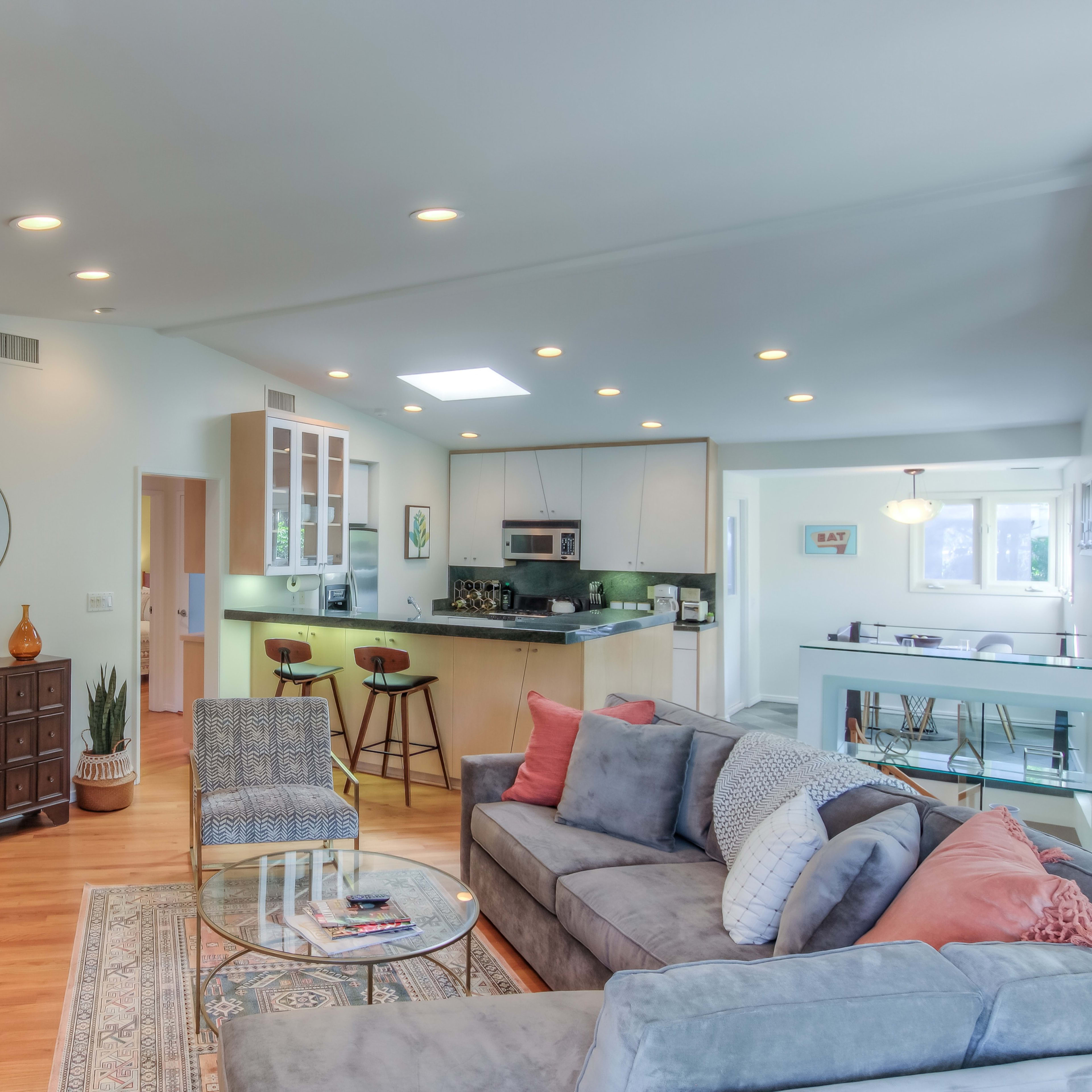 A spacious living room with a modern design, featuring a comfortable sofa, a coffee table, and a fireplace, adjacent to a kitchen area with bar seating.