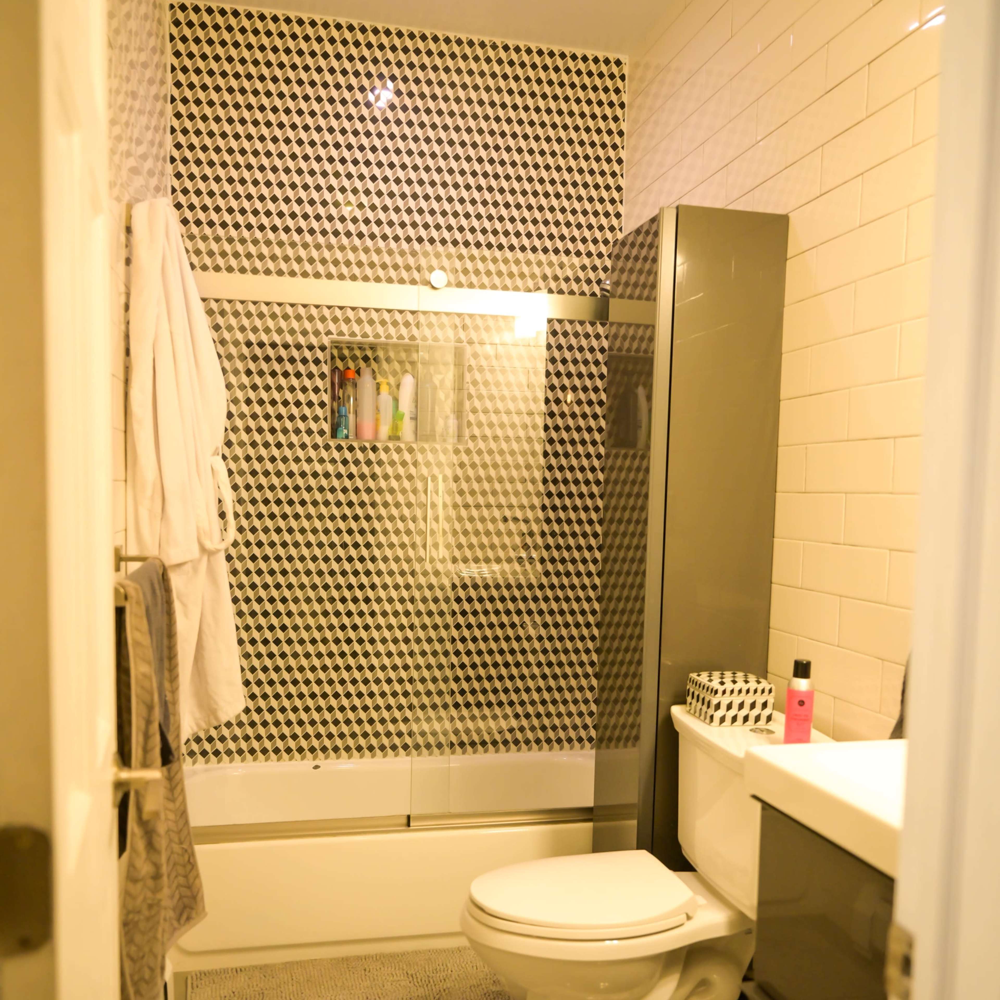 A modern bathroom featuring a shower-tub combination, a toilet, and a vanity with a sink, all surrounded by patterned tile and neutral-colored walls.