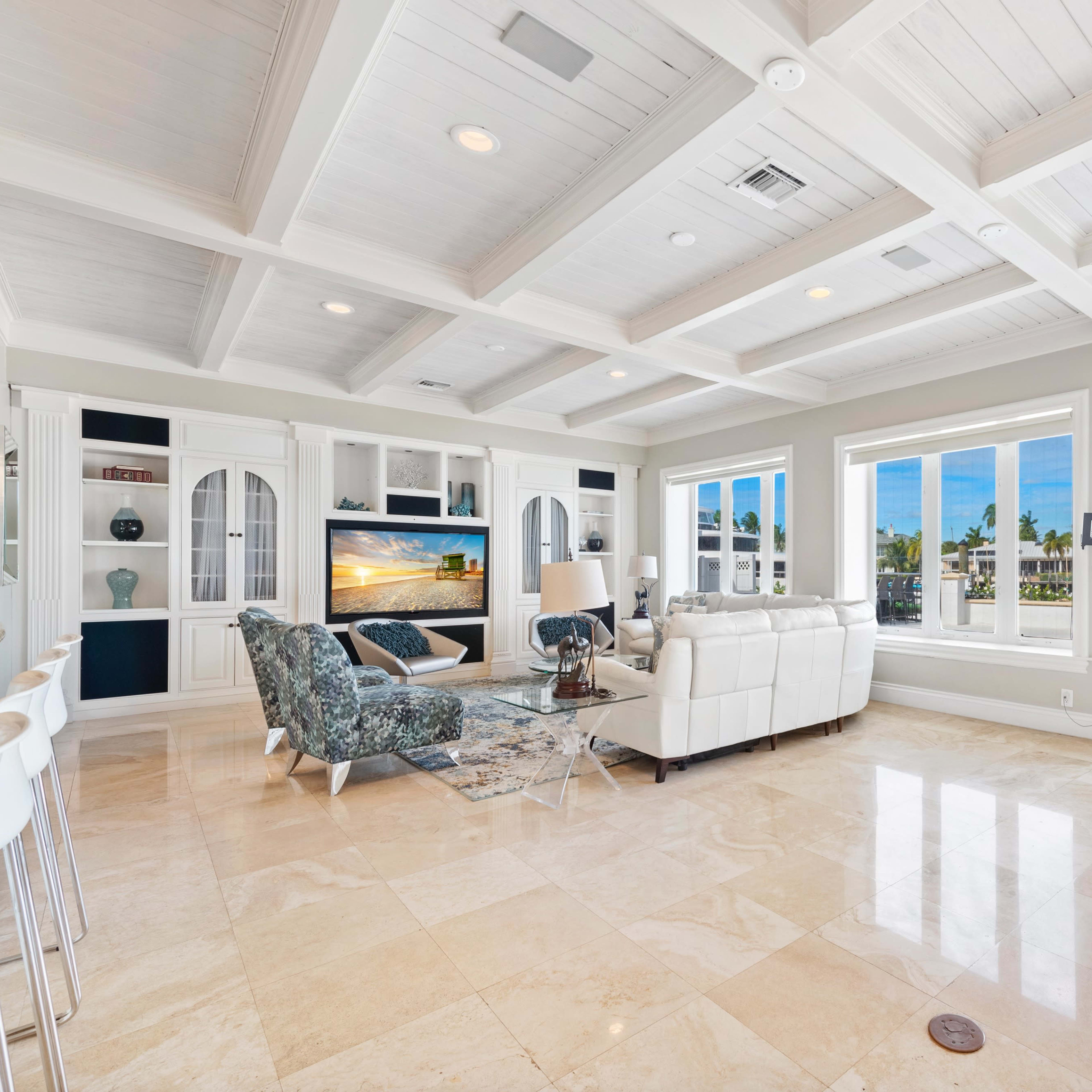 A modern living room with a white leather sofa, a patterned armchair, a coffee table, and large windows that offer a view of an outdoor area.