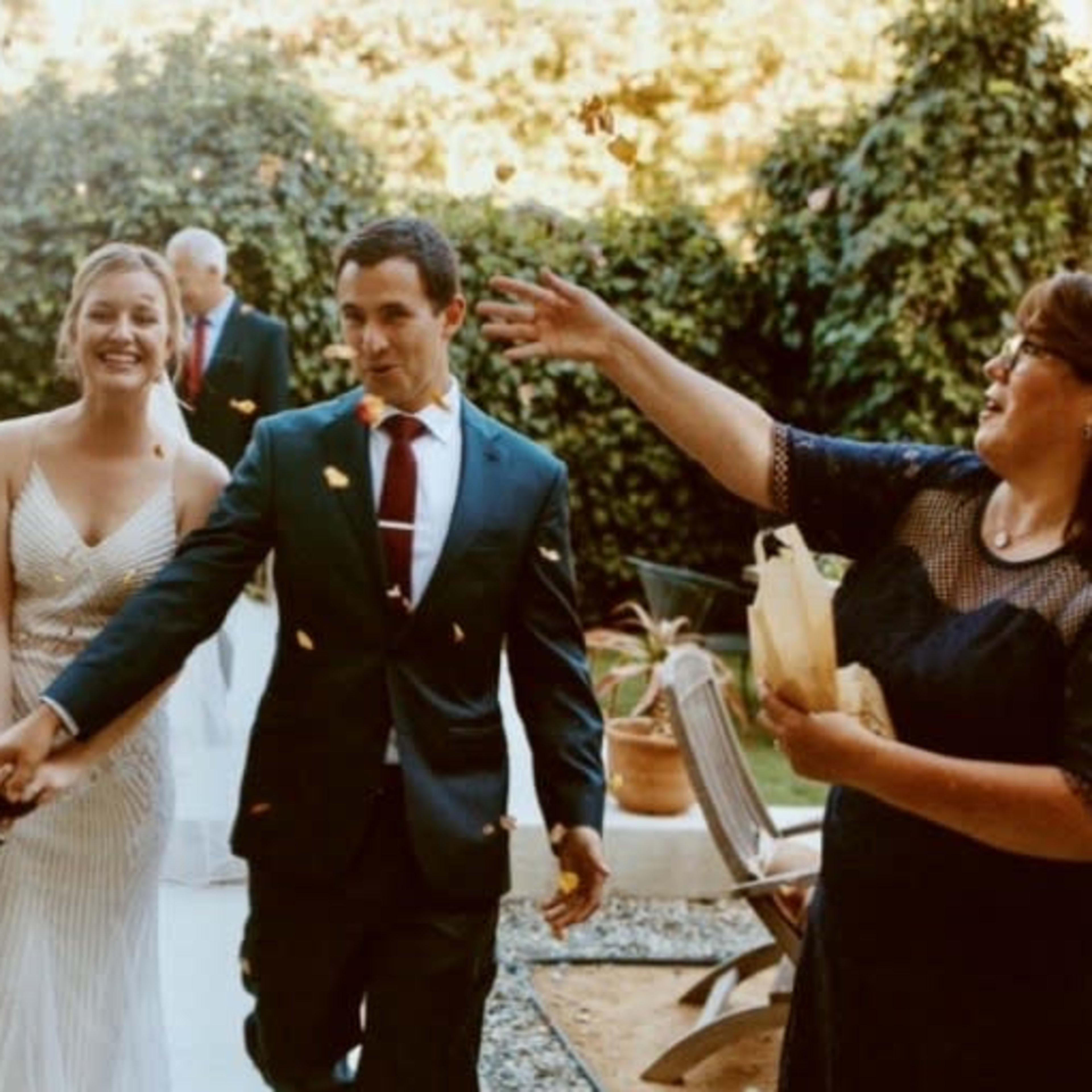 A couple walks hand in hand down a path as guests throw petals in celebration at an outdoor wedding.