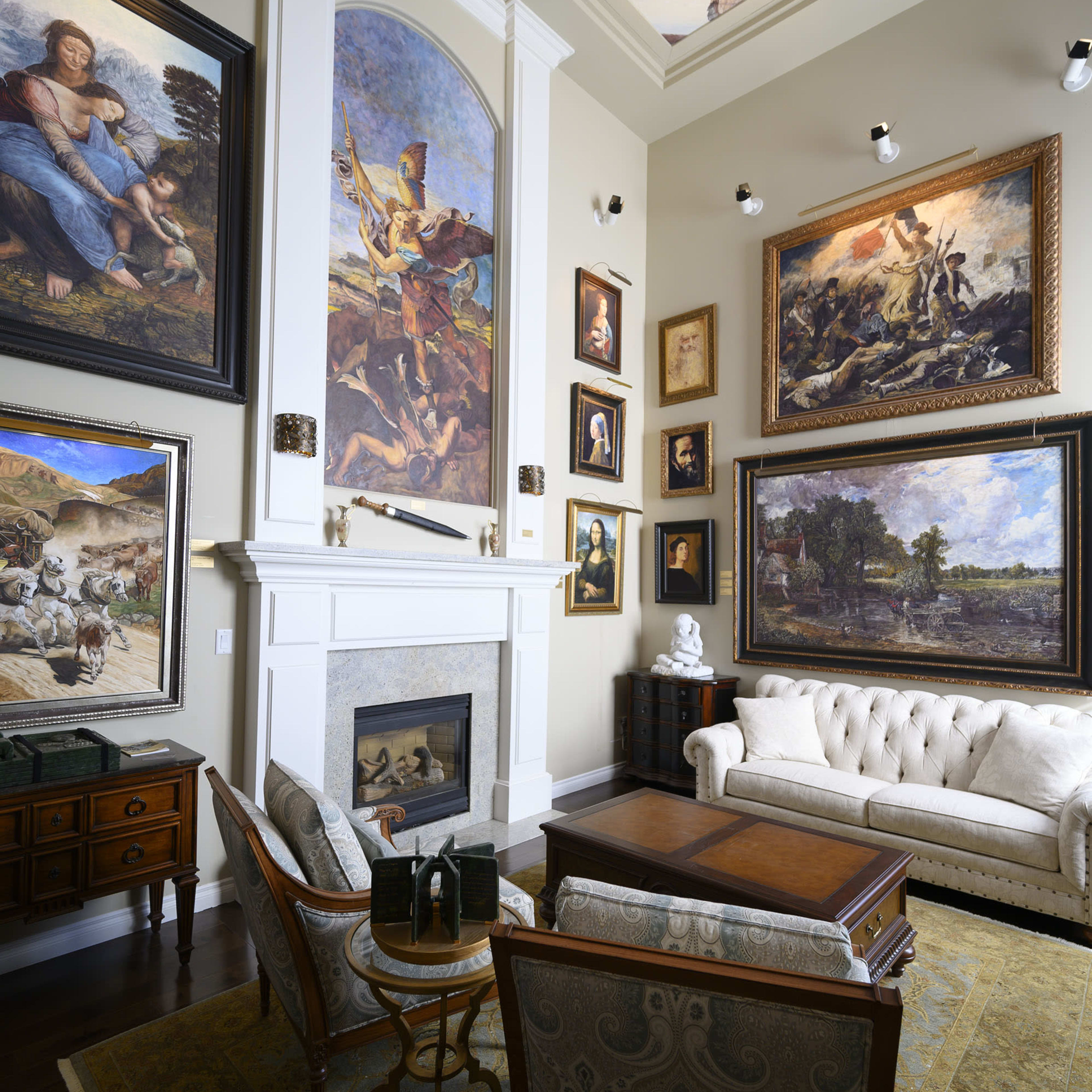 The room features a lavish seating area with a white tufted sofa, a wooden coffee table, and walls adorned with large, framed paintings and a decorative ceiling.
