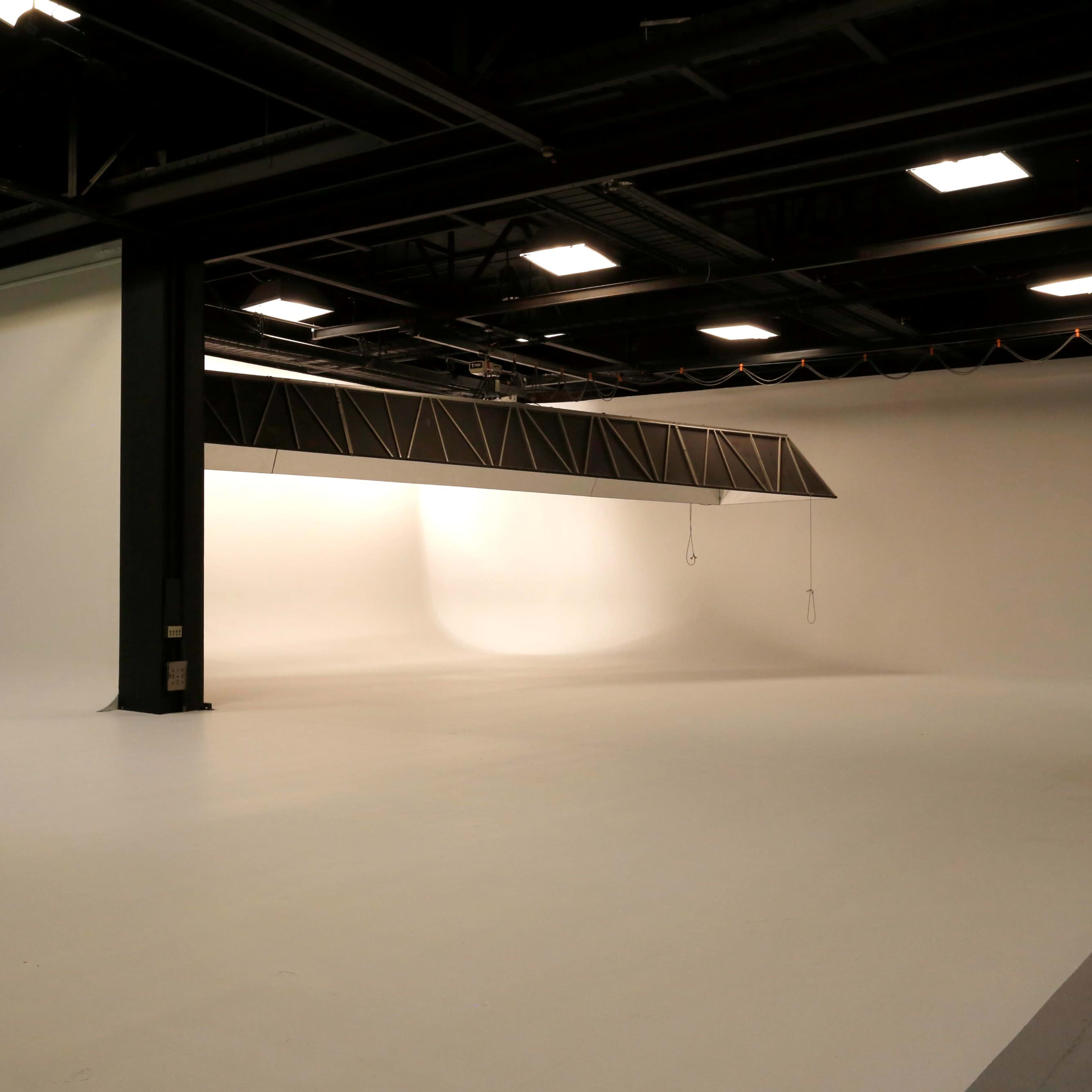 An empty film studio with a white backdrop, large space, and a few director's chairs arranged on one side.