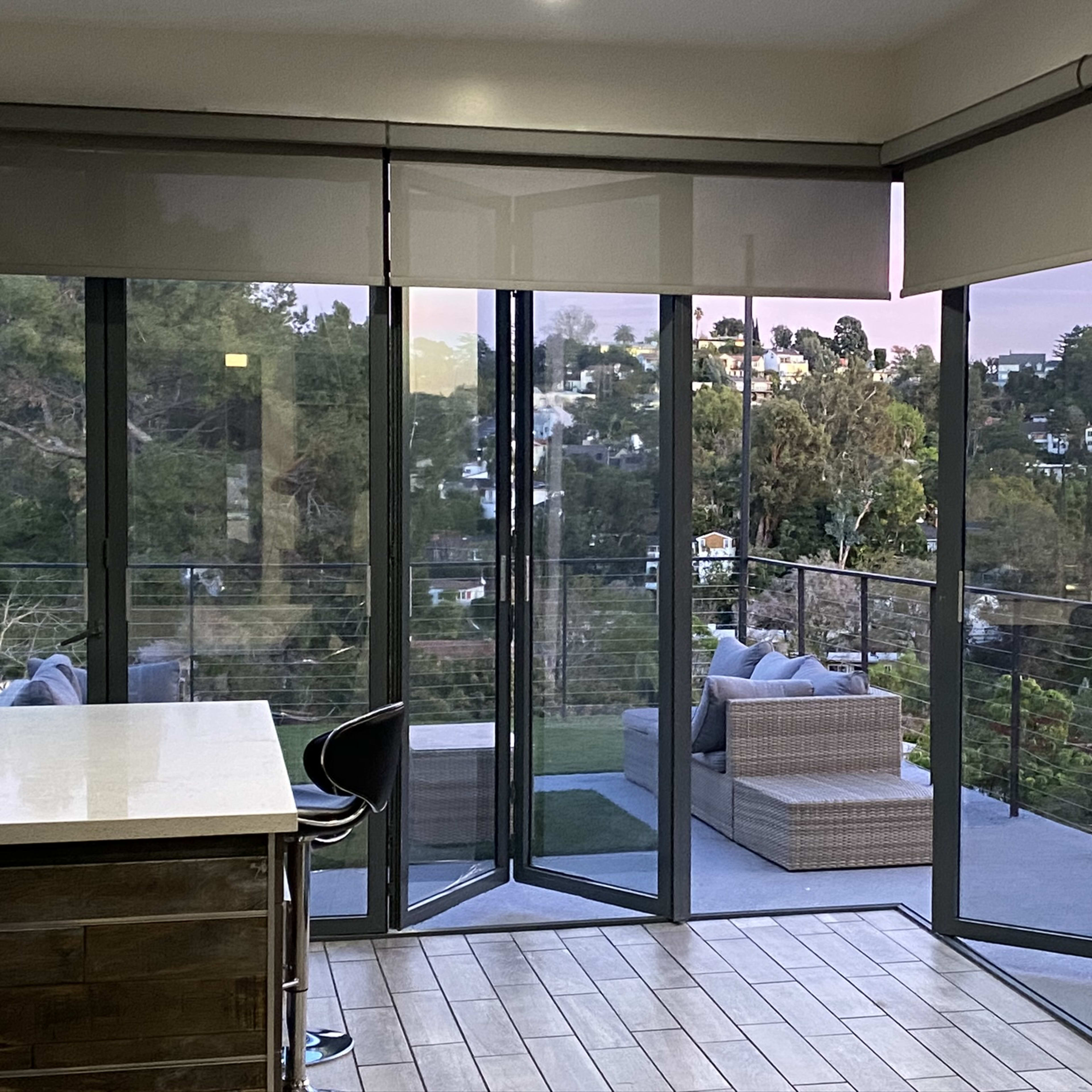 A modern interior space with large glass sliding doors opening to a patio area surrounded by greenery.