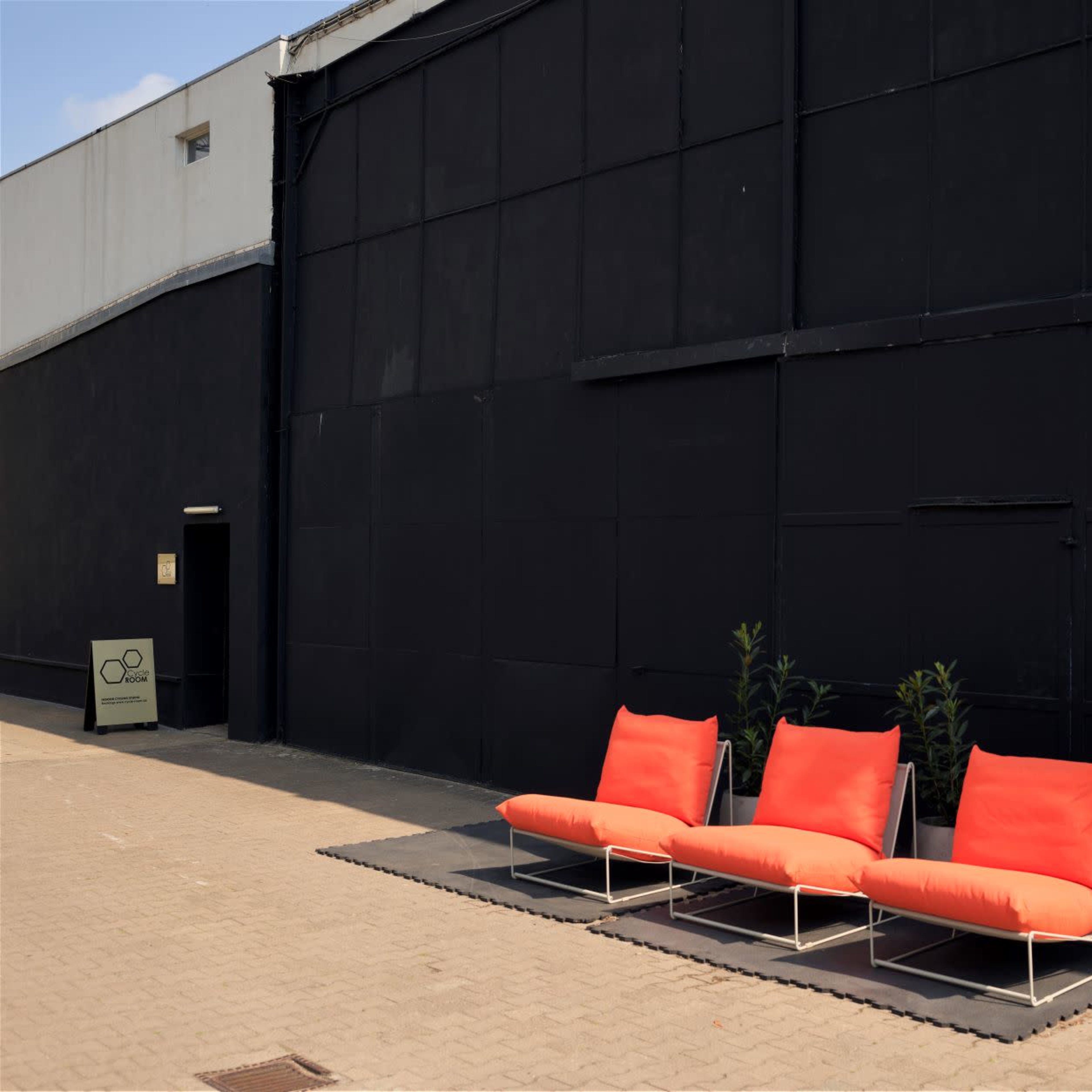Three orange lounge chairs arranged on a black surface in front of a black wall and an open garage door.