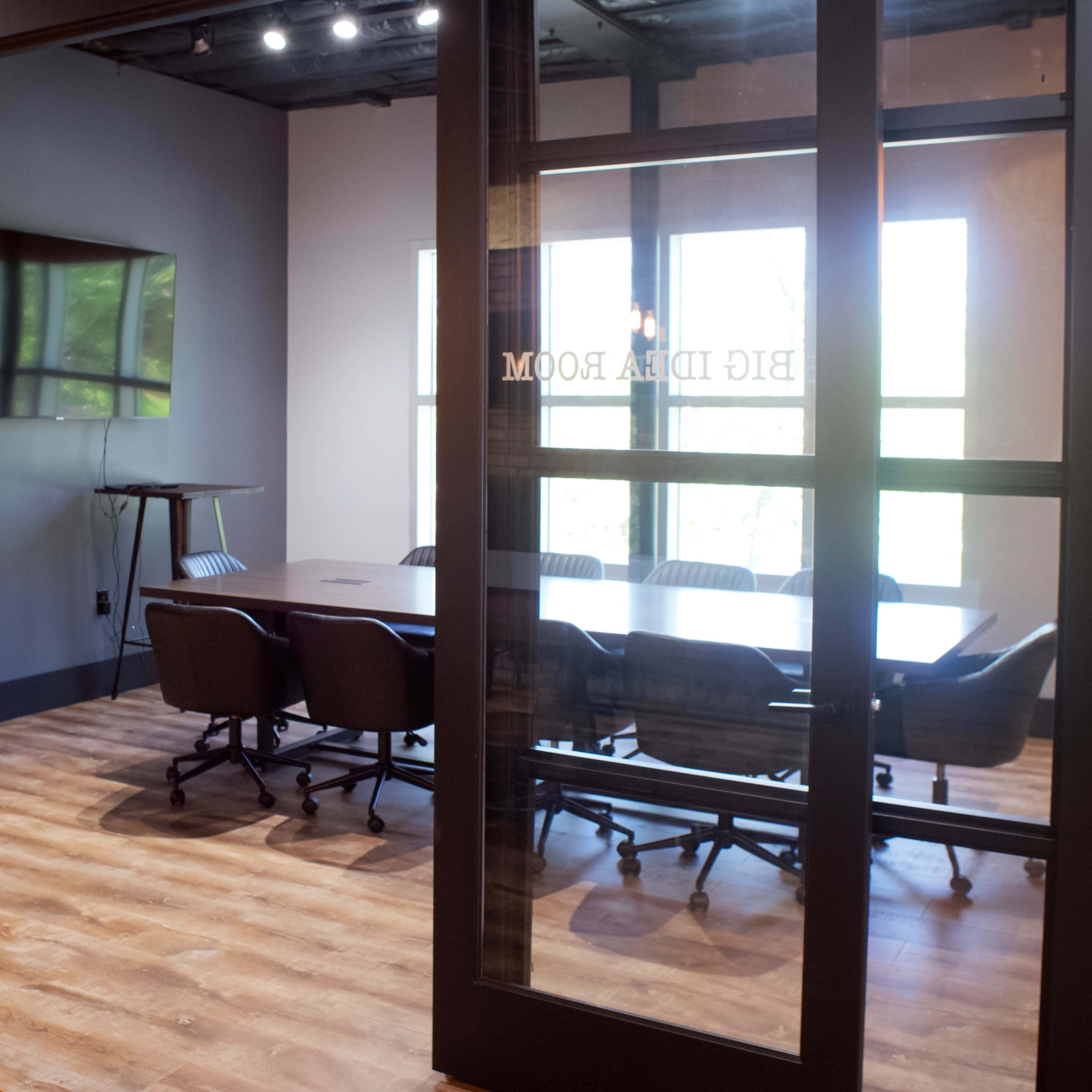 A modern conference room with a large table surrounded by several chairs, visible through glass doors.