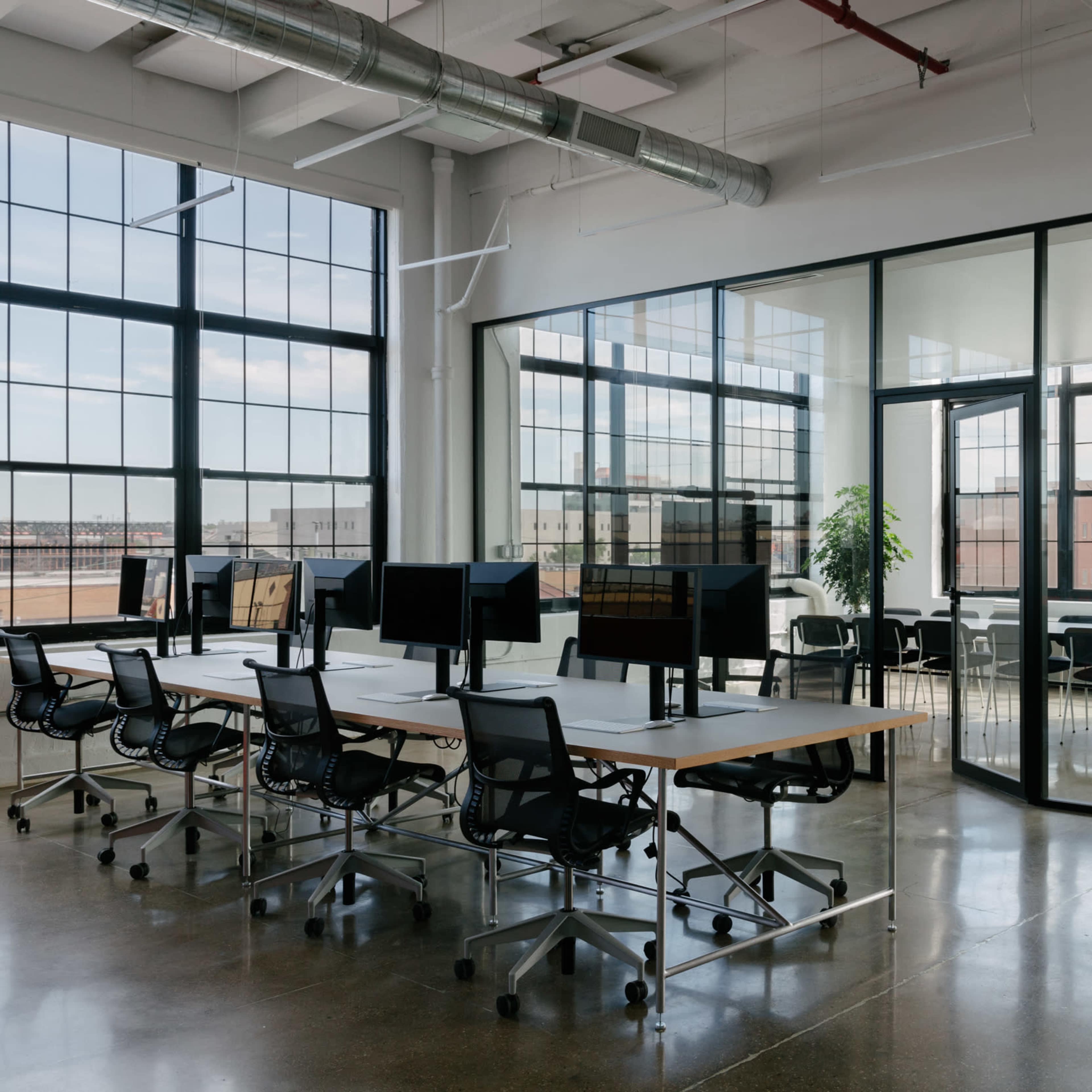 A modern office space featuring a row of desks with computer monitors and a glass-walled meeting room.