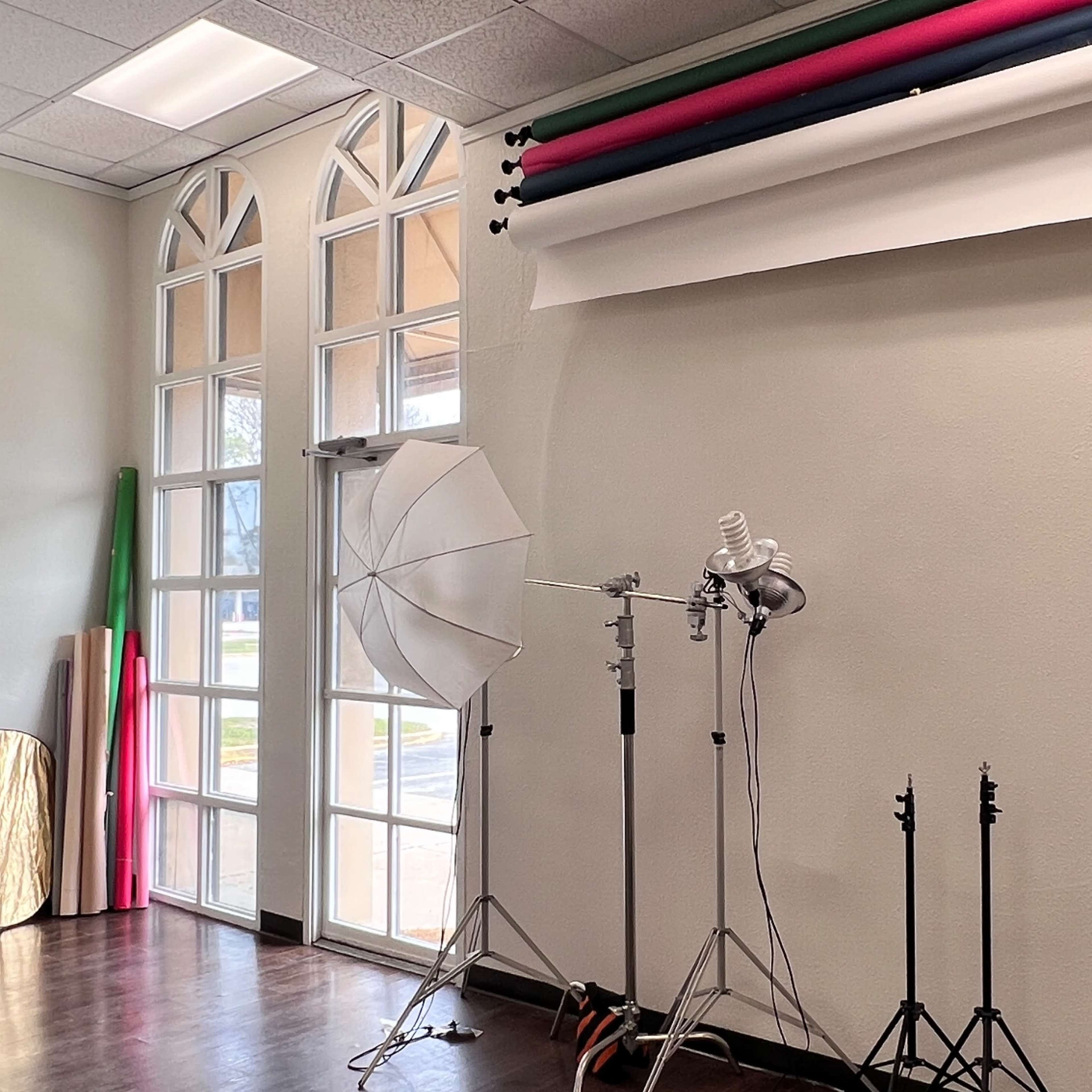 A photography studio with background rolls, lighting equipment on stands, and a large reflector against a neutral wall.