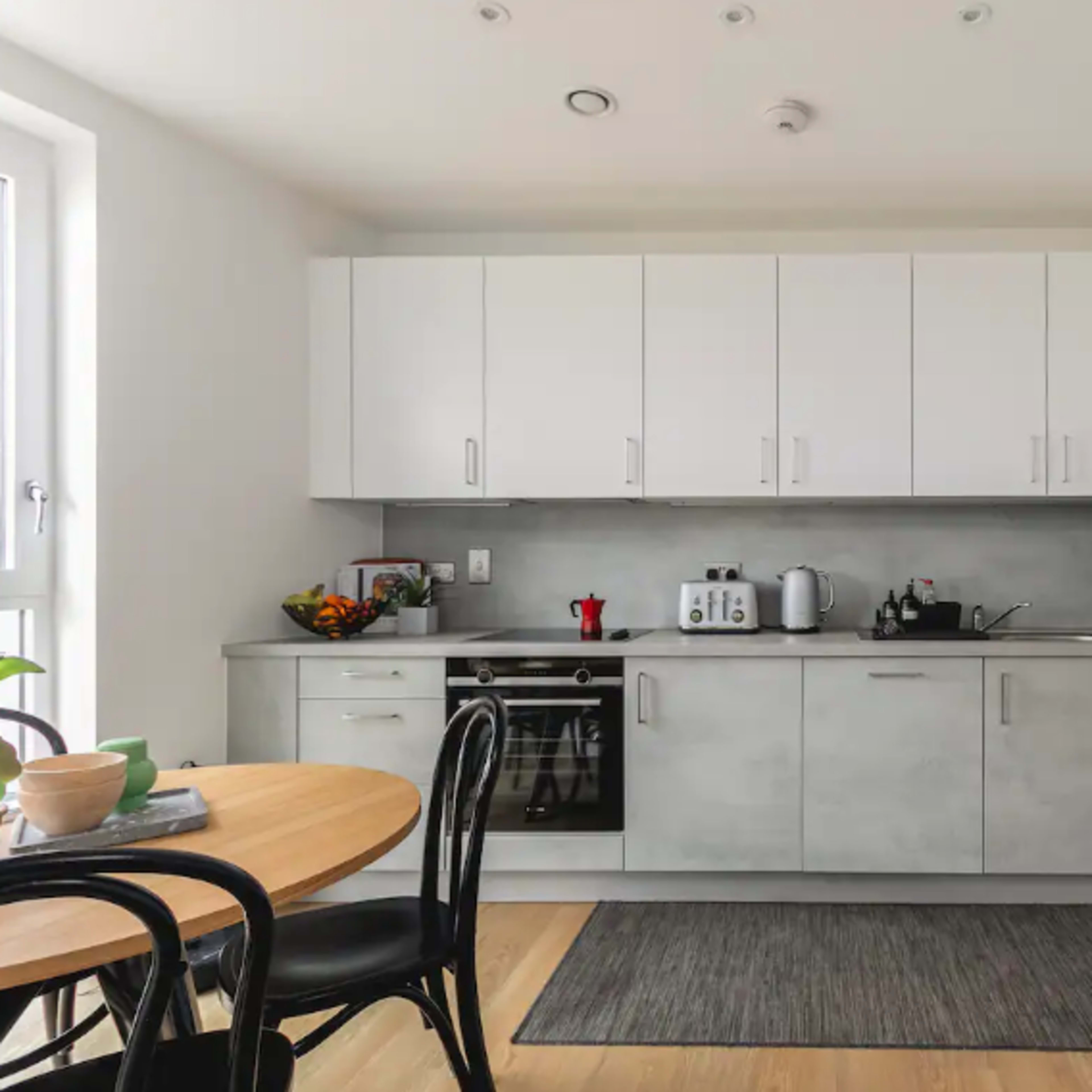 A modern kitchen features light gray cabinetry, a black stove, and a round dining table with black chairs.