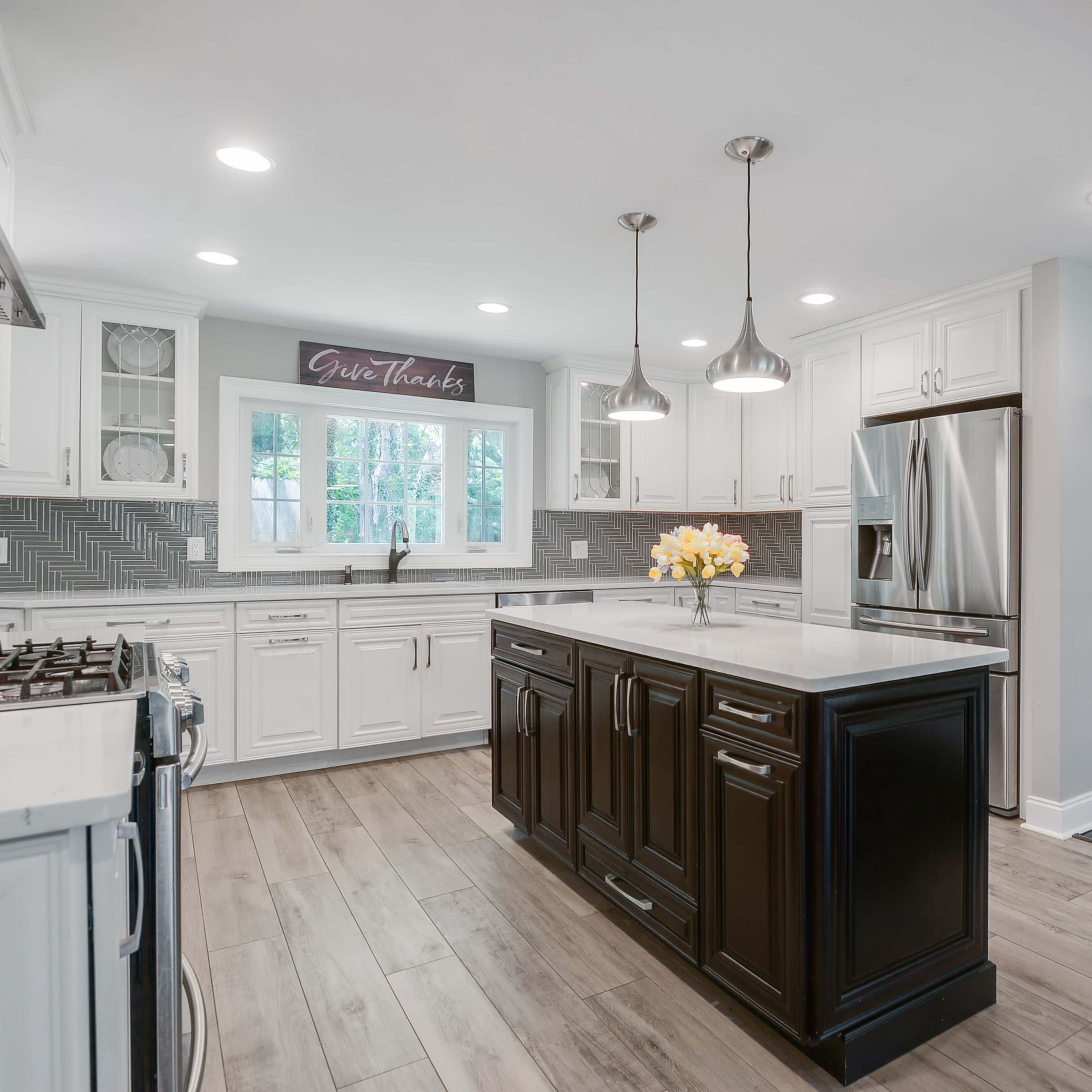 A modern kitchen with white cabinets, a dark island, and stainless steel appliances, featuring a central island with a floral arrangement.