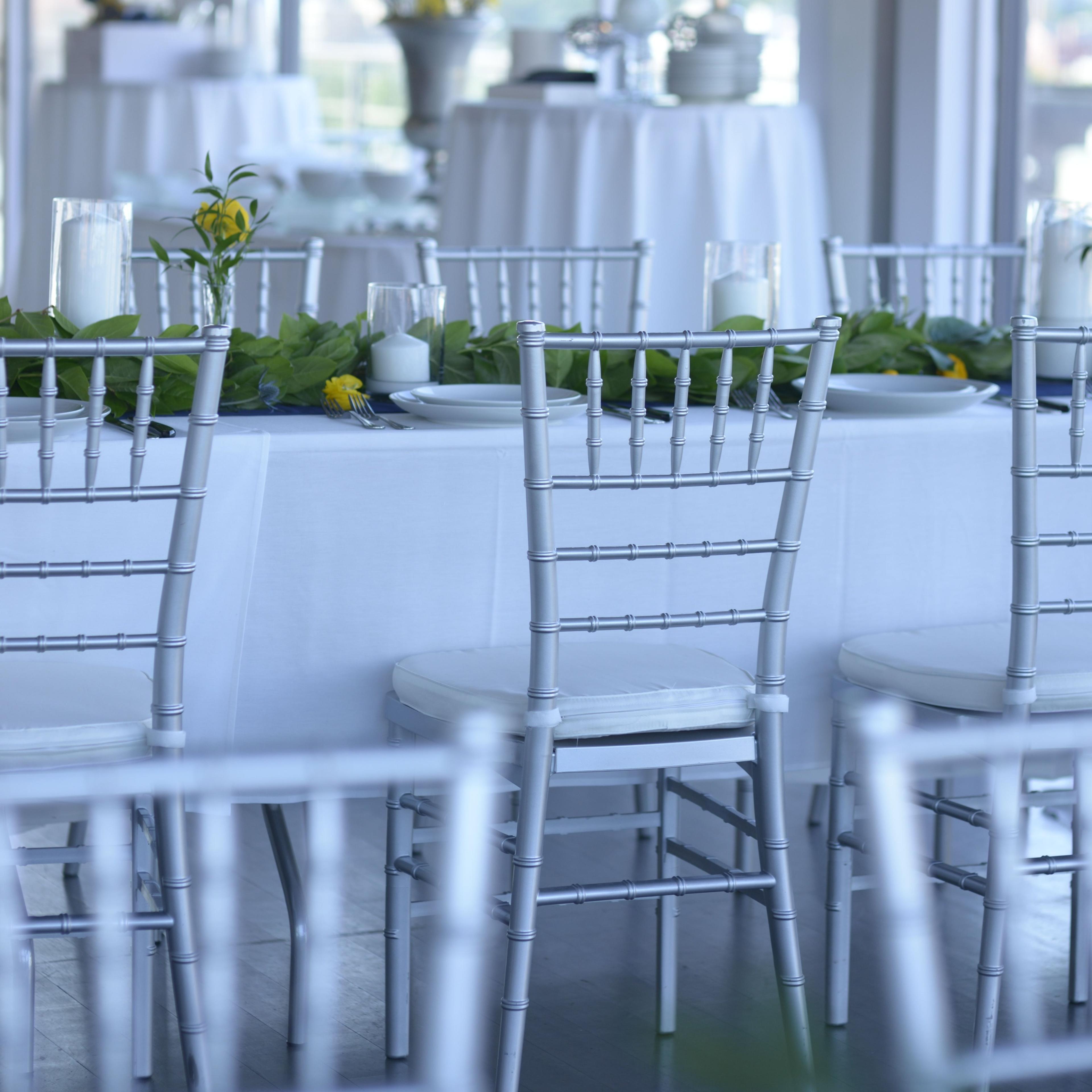 A spacious banquet room features tables set with white tablecloths and adorned with leafy centerpieces and drinks.