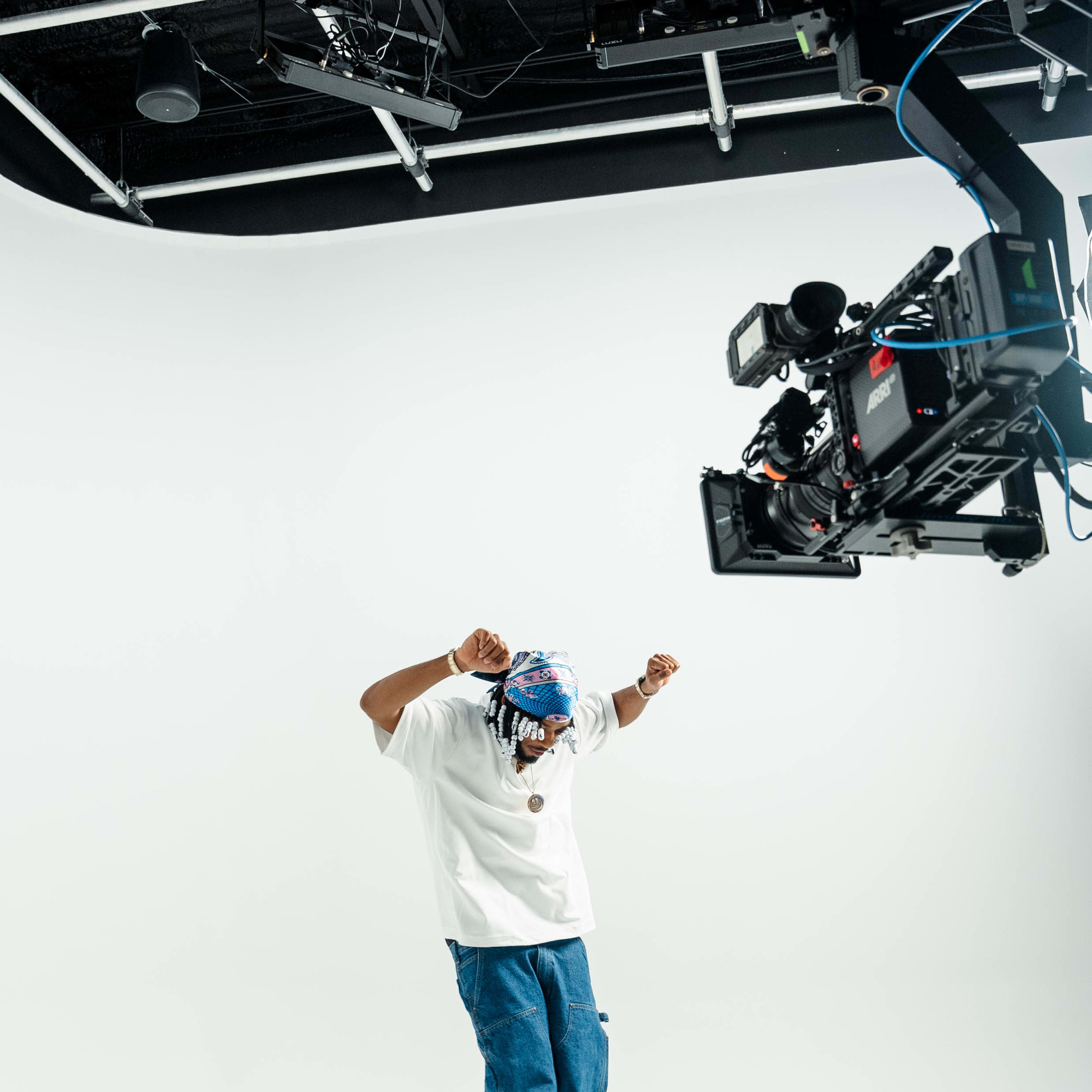 A person wearing a white shirt and blue jeans dances under a camera suspended from a rig.