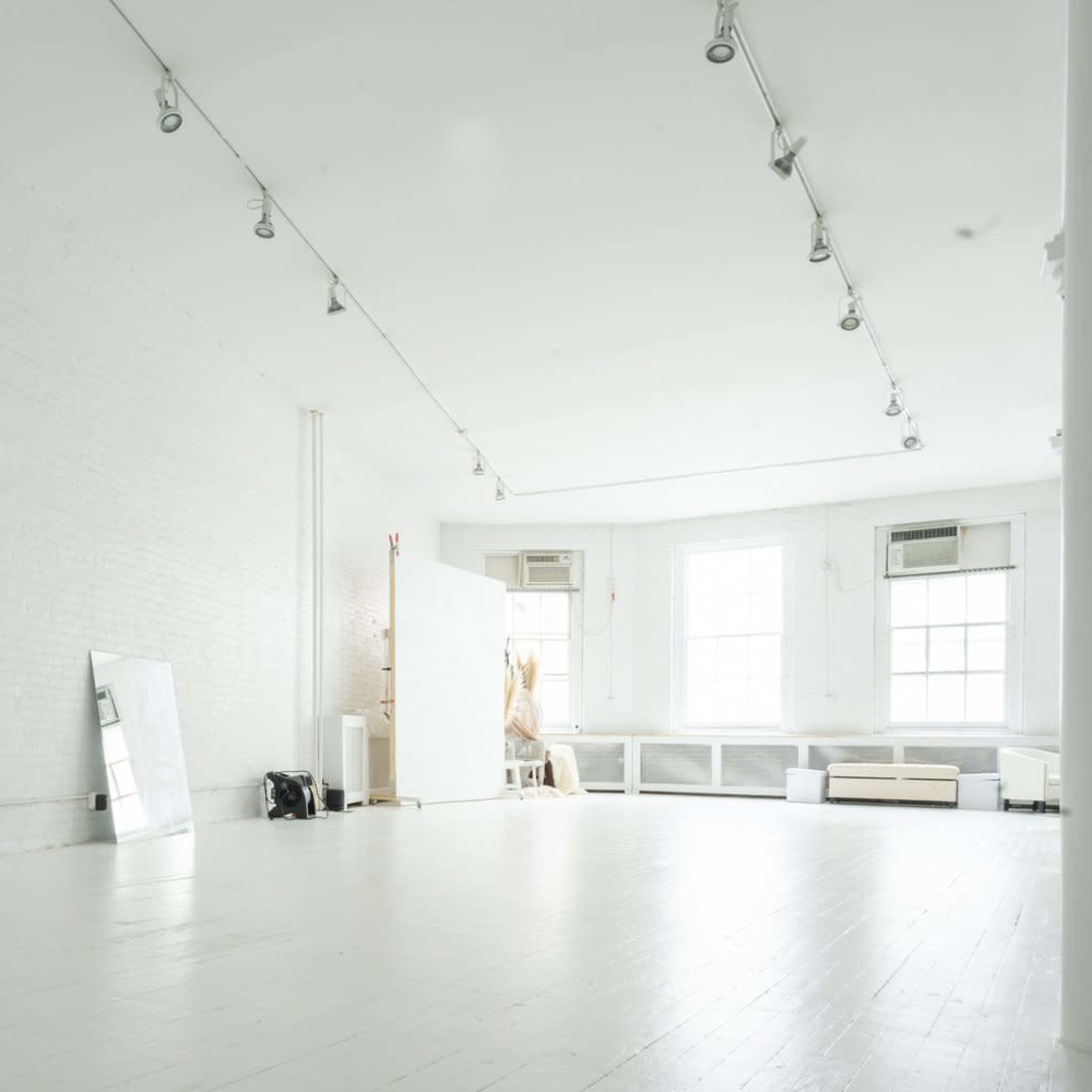 A spacious, empty studio with white brick walls, hardwood floors, and large windows.