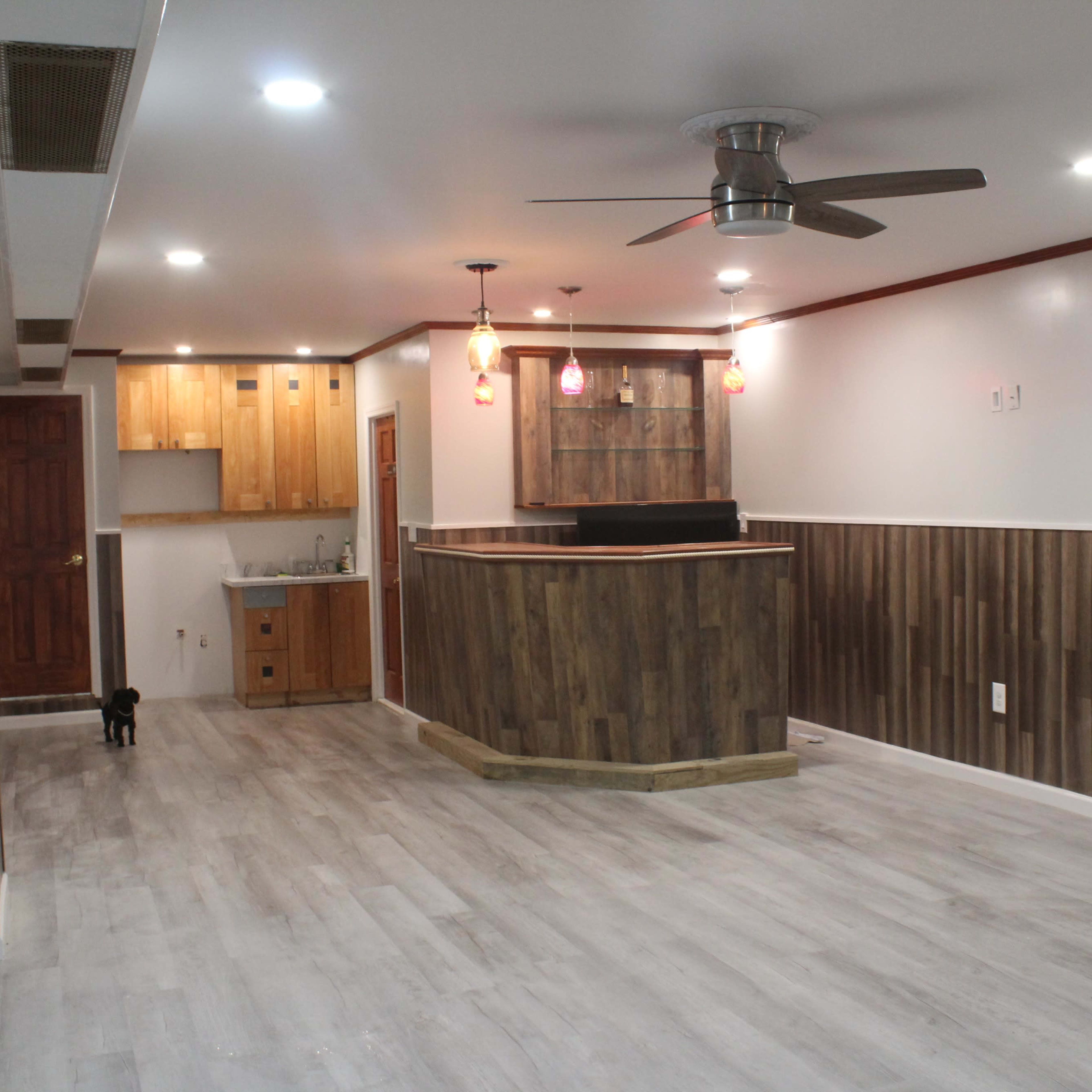 A spacious, modern room featuring a wooden bar area with pendant lighting and laminate flooring.