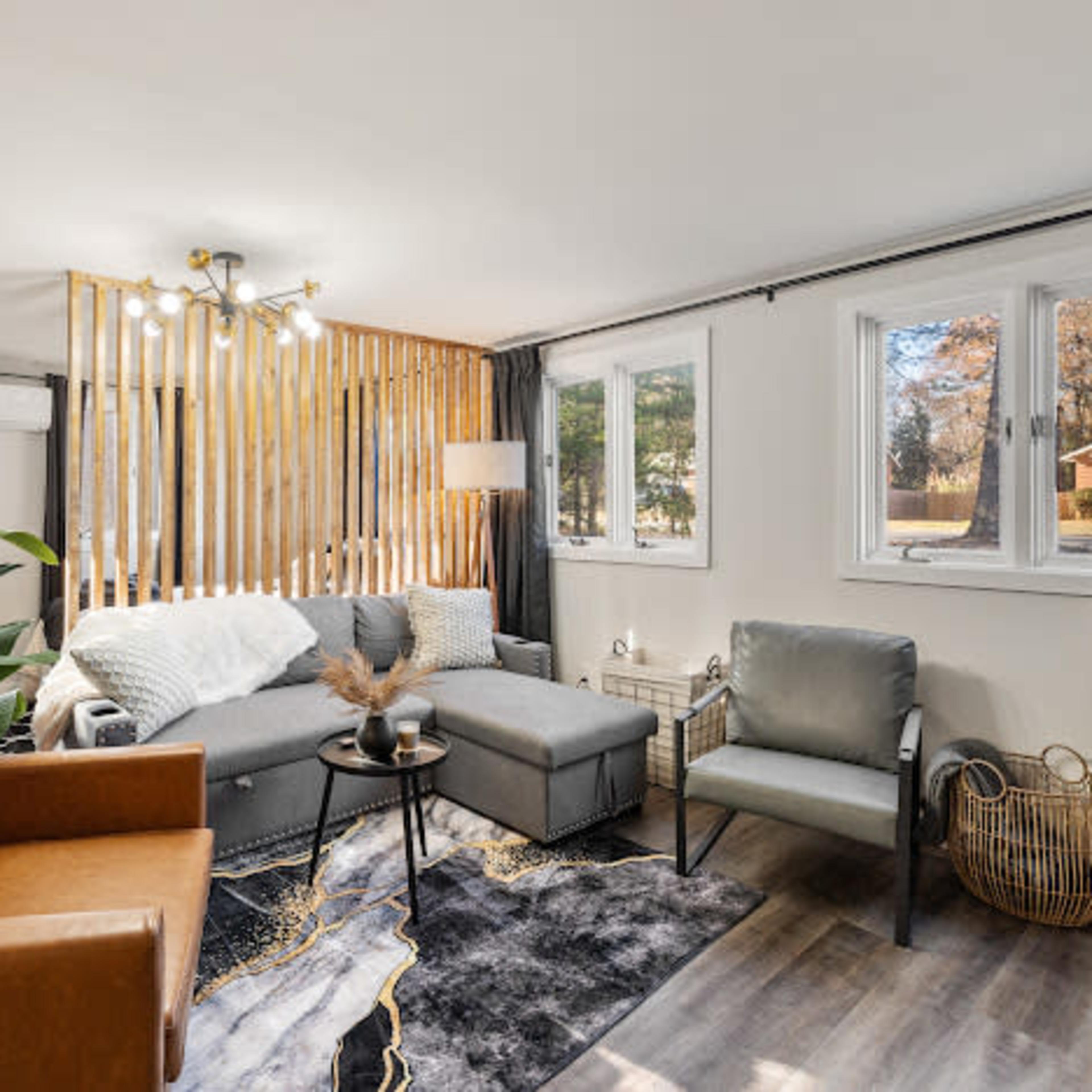 A modern living room featuring a sectional sofa, a brown leather chair, light wood paneling, and large windows providing natural light.