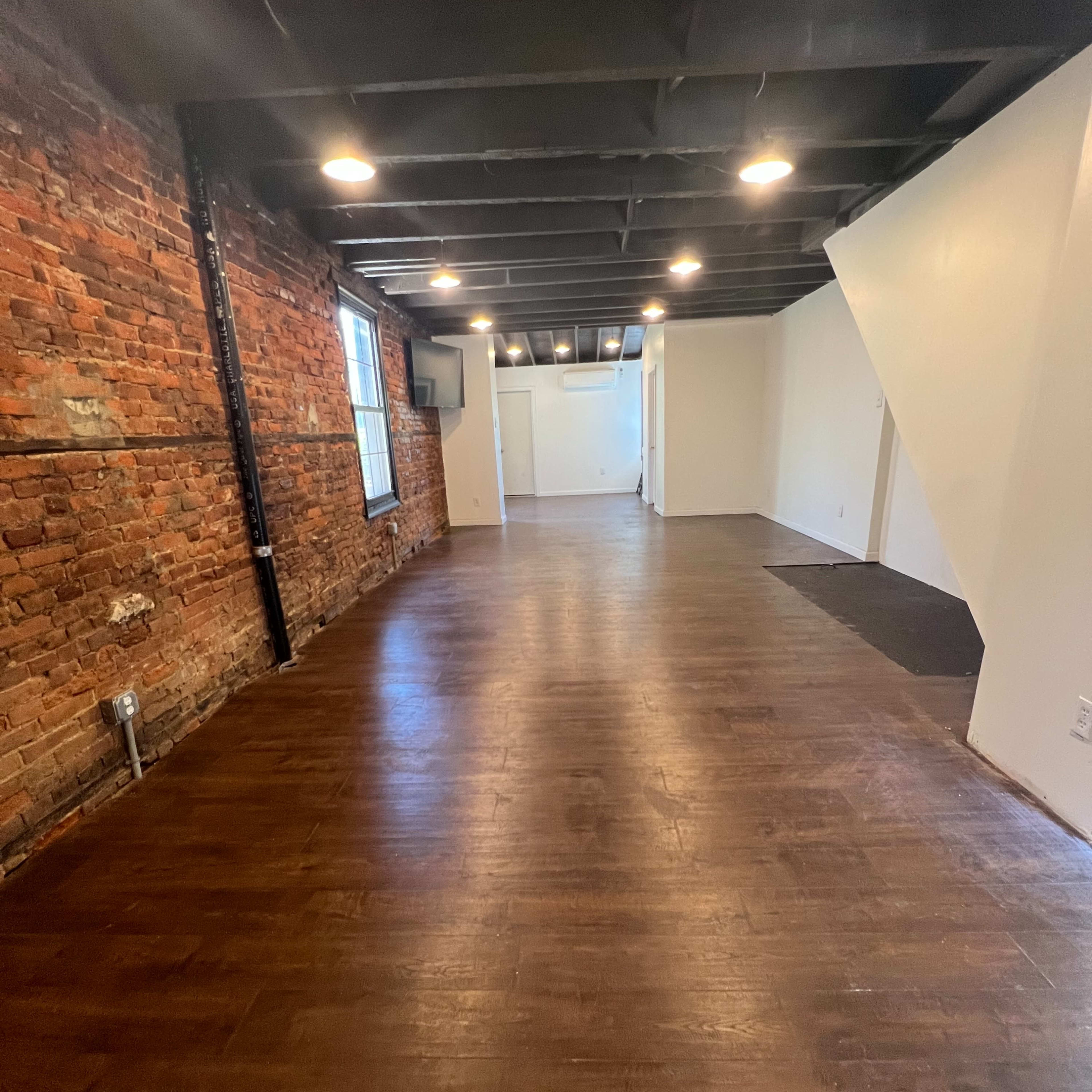 A spacious, empty interior room featuring exposed brick walls and hardwood flooring.