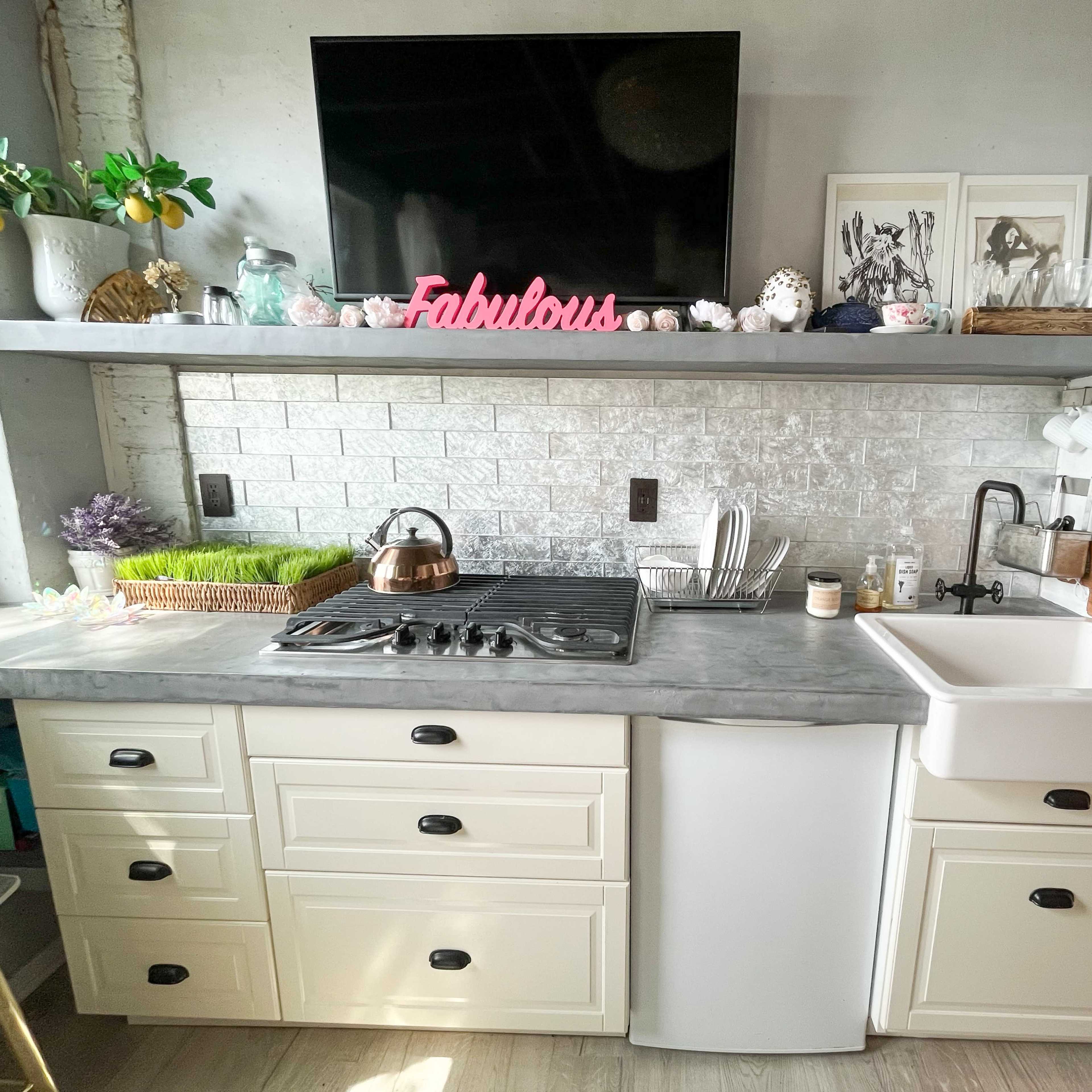 A modern kitchen area with a gas stove, a farmhouse sink, a television mounted on the wall, and decorative items on the open shelf above the countertop.