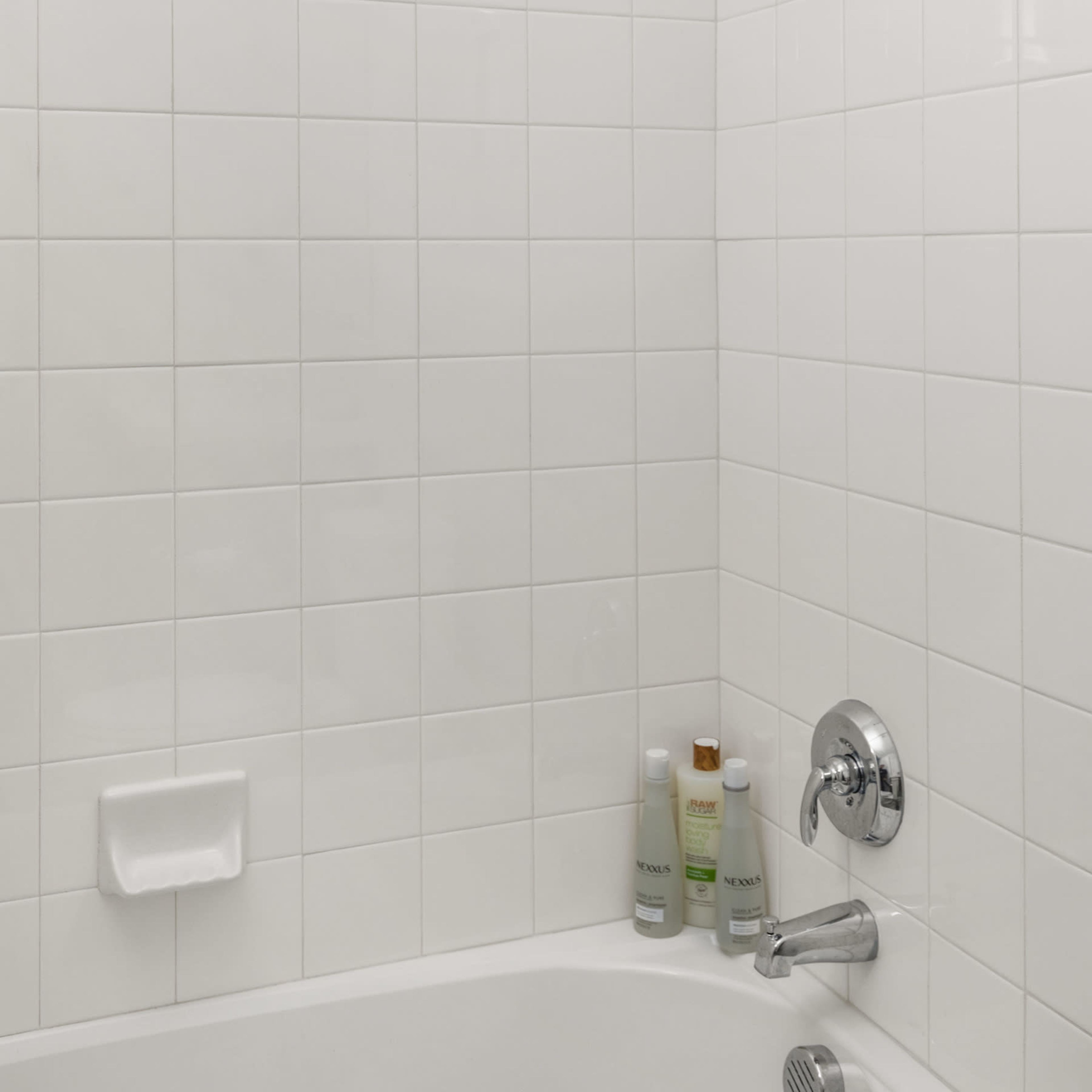 A clean, tiled shower stall with a wall-mounted showerhead and a few bottles of shampoo placed on the ledge.