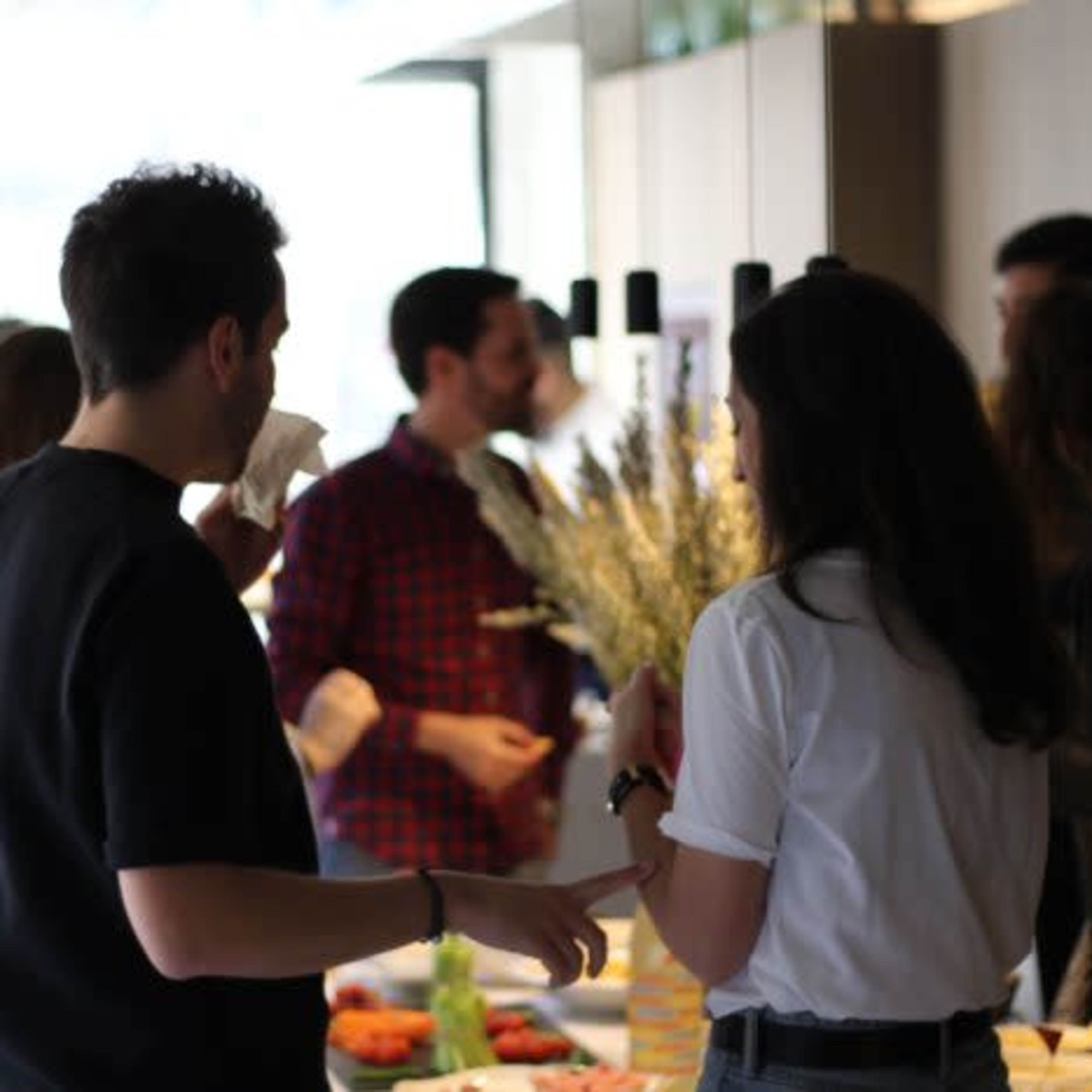 A group of people socialize around a buffet table in a brightly lit indoor setting.