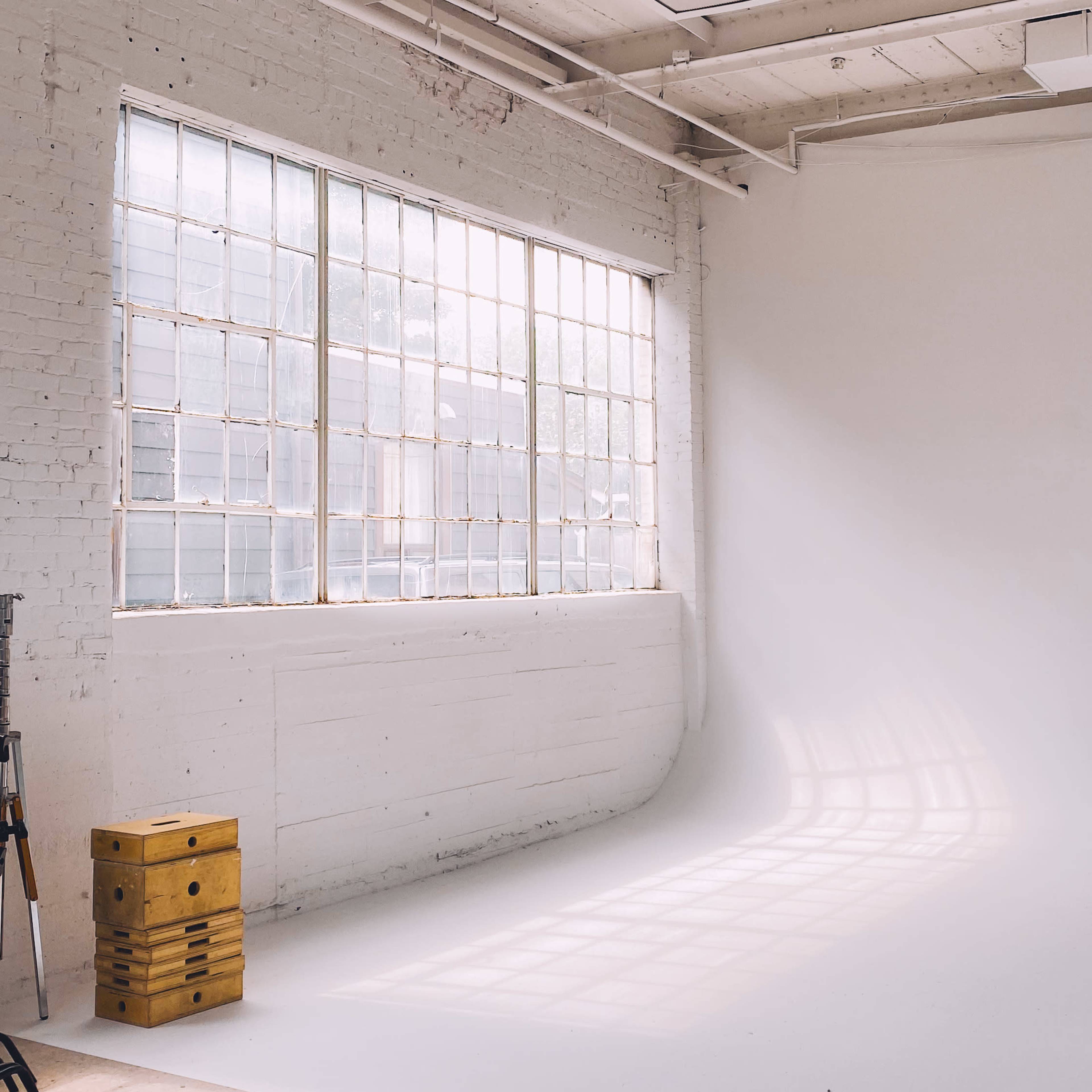 A spacious, well-lit studio with large windows and a white backdrop.