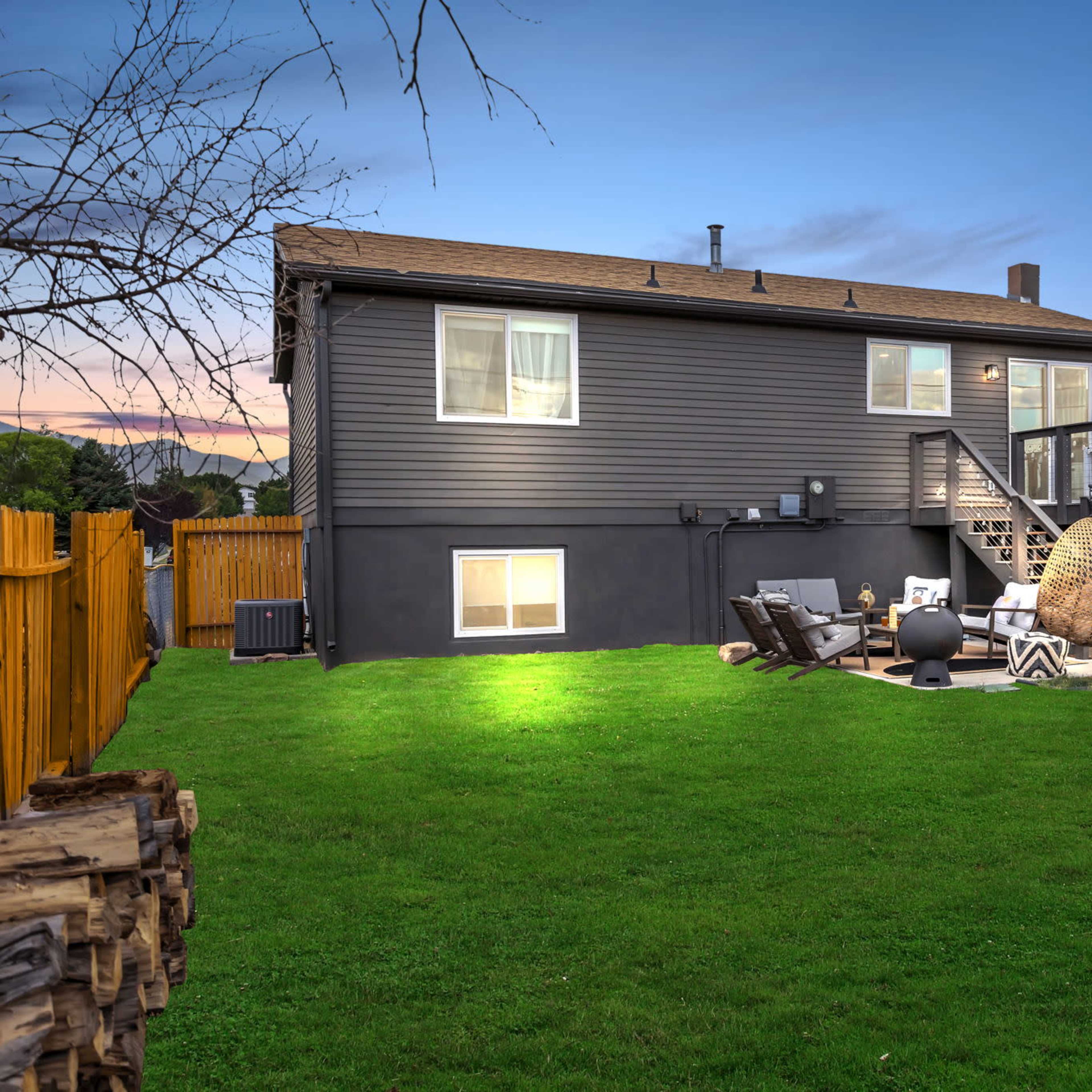 A two-story gray house with a wooden deck and a spacious backyard featuring outdoor furniture and a fire pit.
