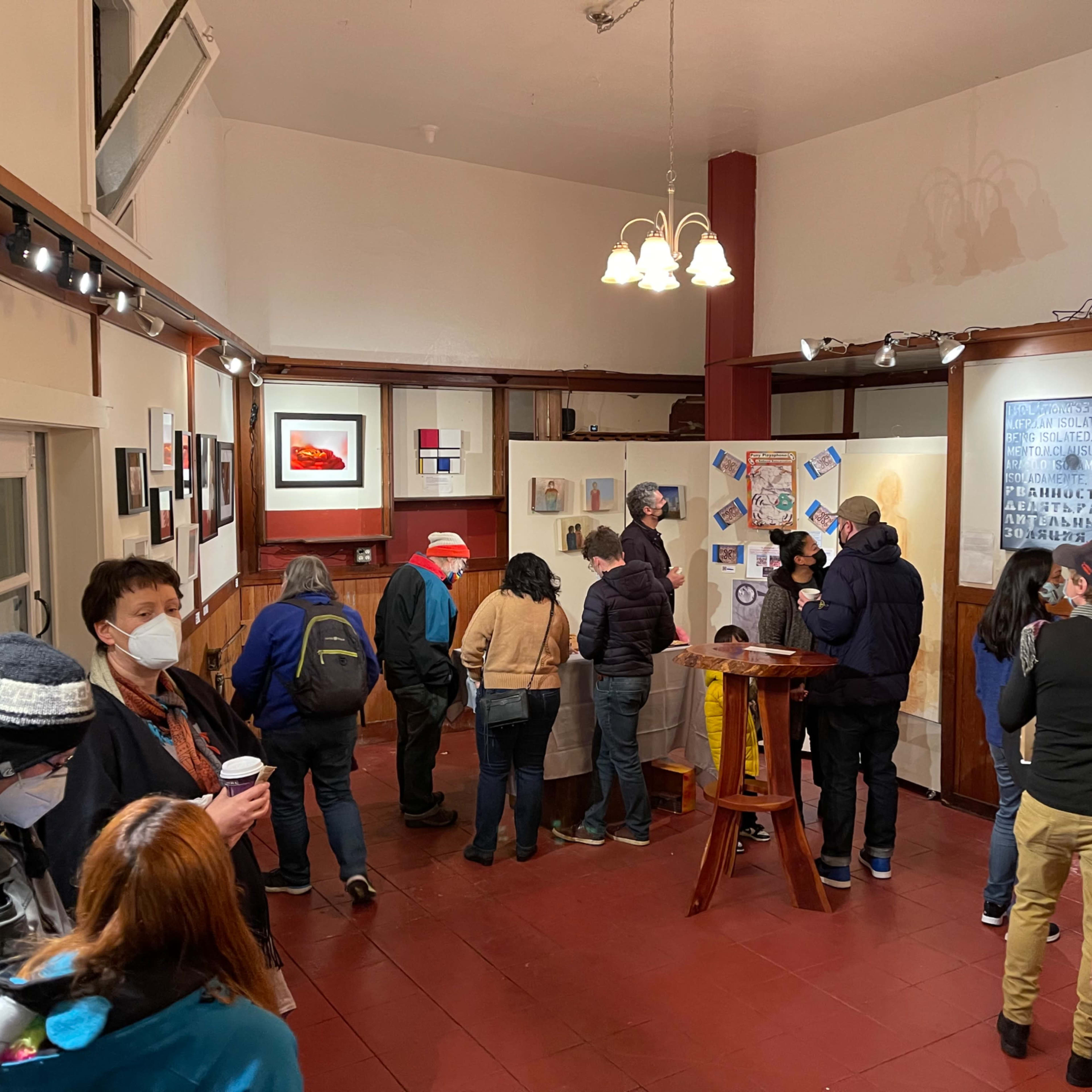 A group of people gathers in an art gallery, viewing various artworks displayed on the walls.