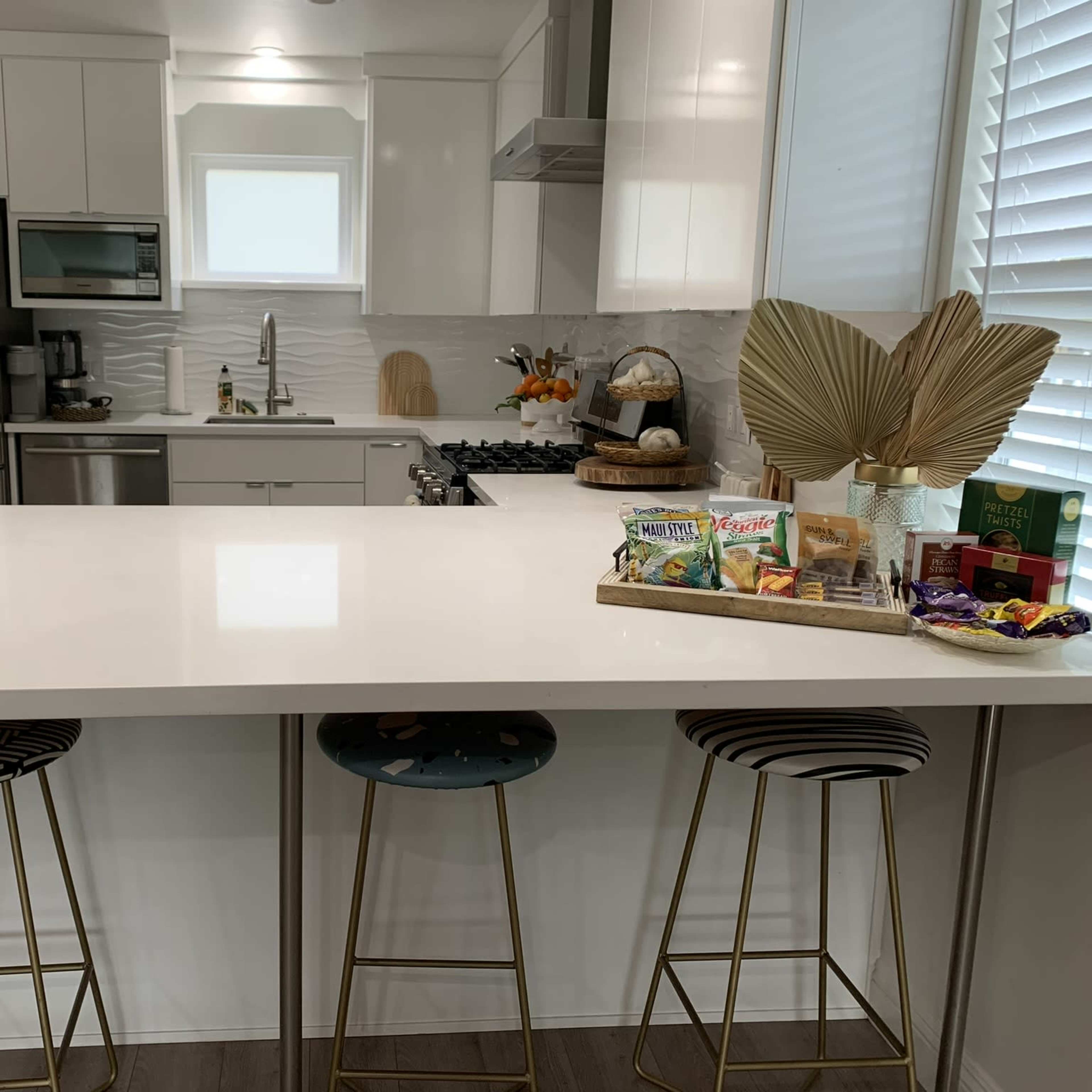 A modern kitchen with a white countertop, stainless steel appliances, and three decorative bar stools.