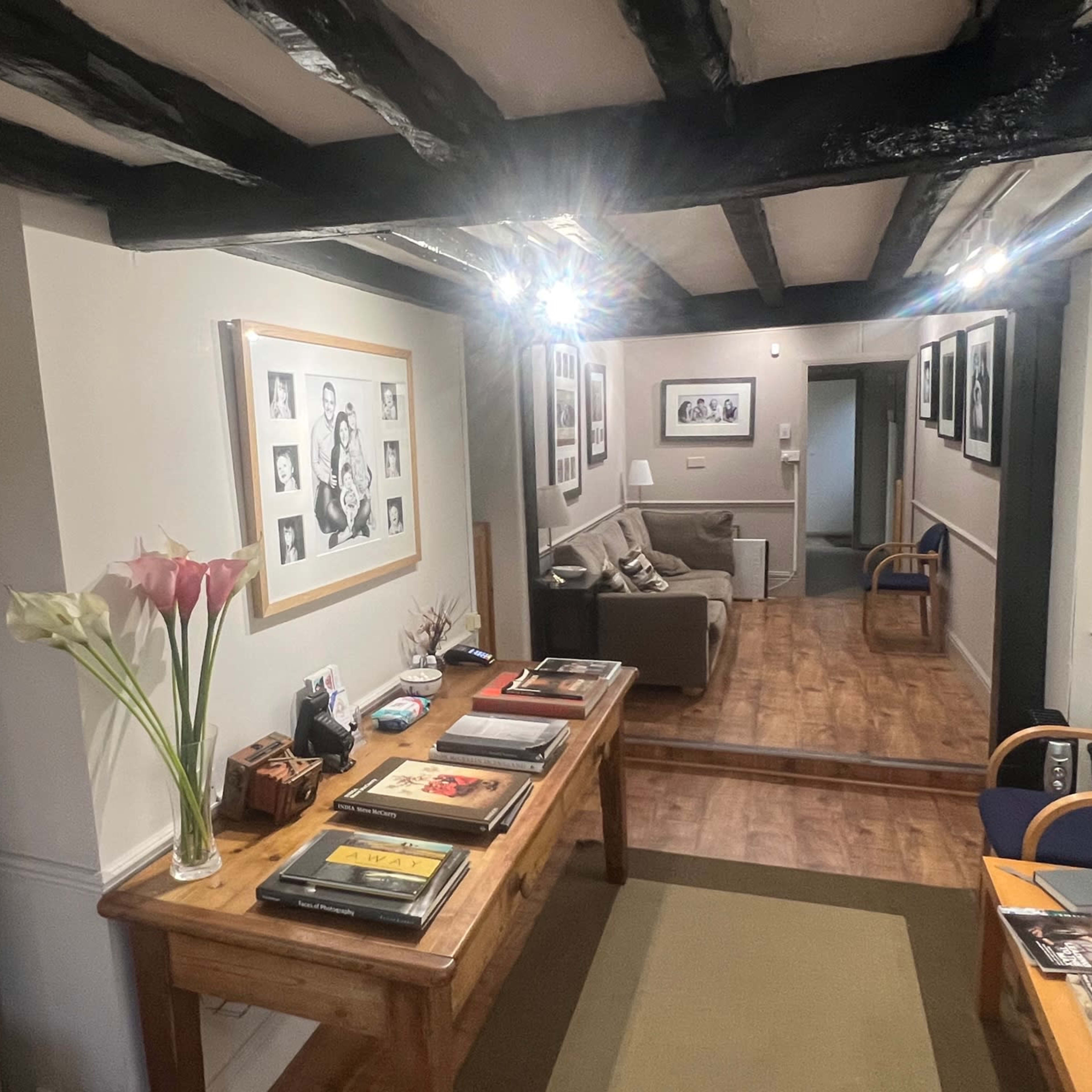 A reception area with a wooden table displaying magazines, flanked by seating areas and framed photographs on the walls.