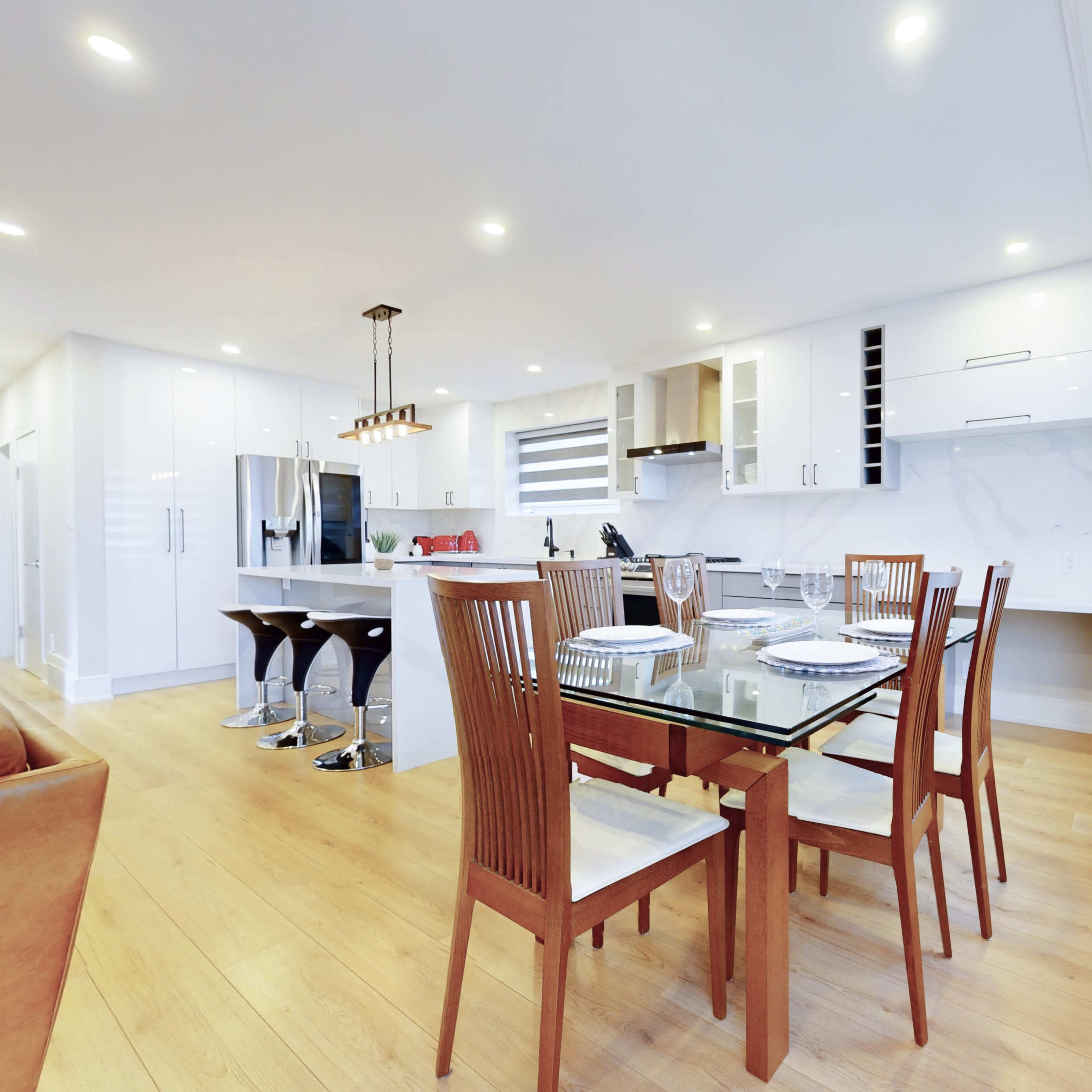 A modern kitchen and dining area featuring a glass-top table with wooden chairs, a marble countertop, and stainless steel appliances.